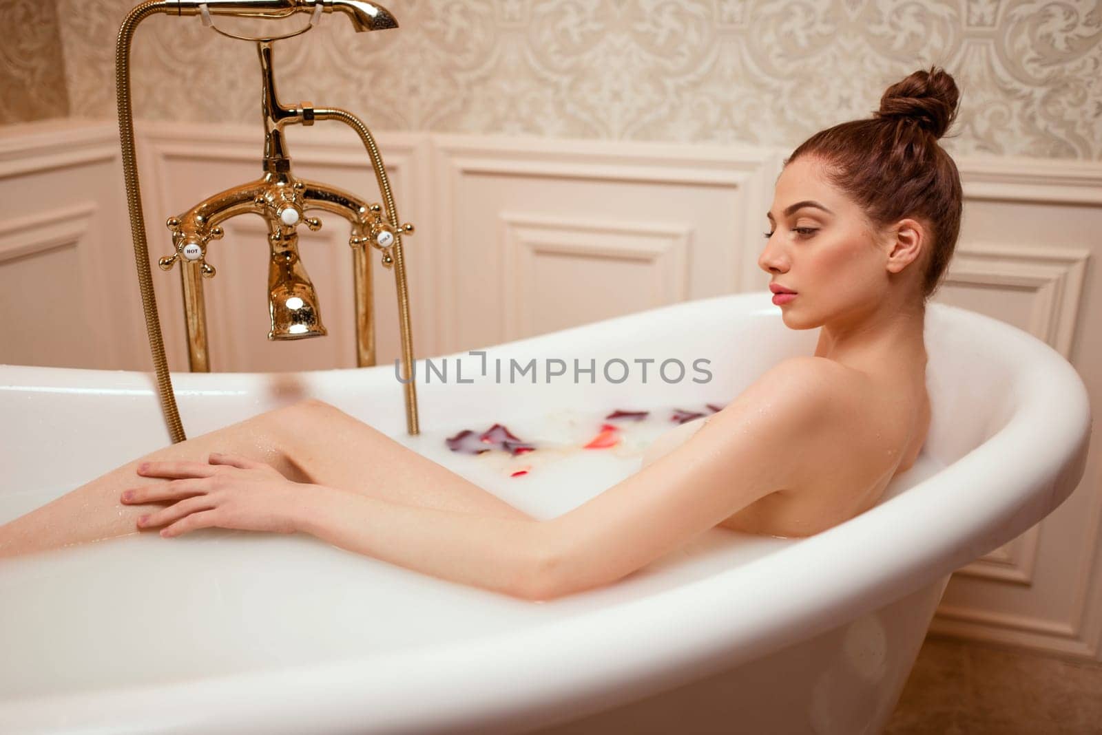 Beautiful woman in bath with rose petals and foam.