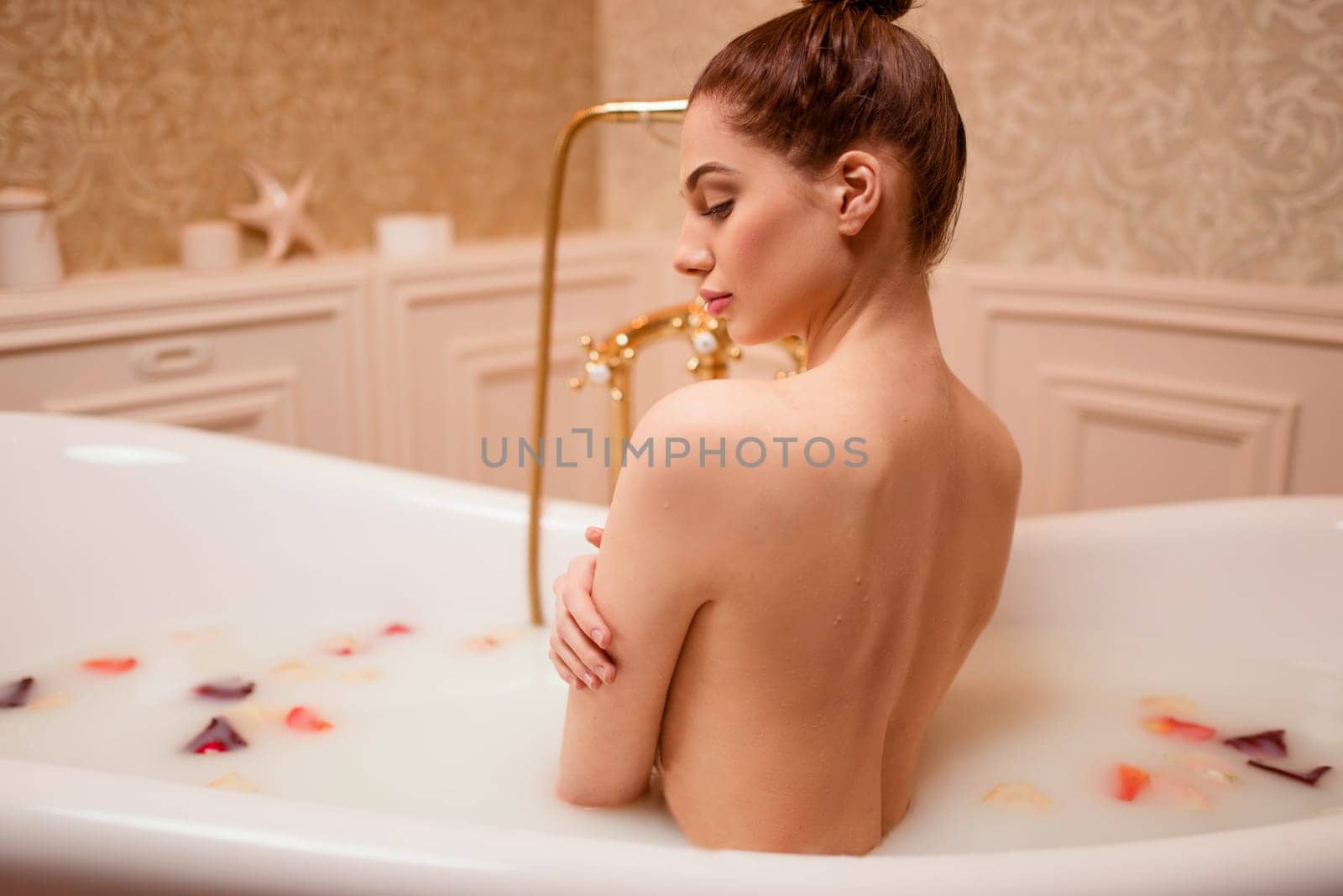 Beautiful nude woman in bathtub with rose petals and foam.