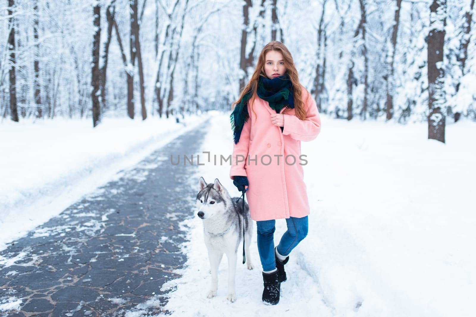 Young woman walks in the park with siberian husky, snowy forest on background. Cute girl with charming dog
