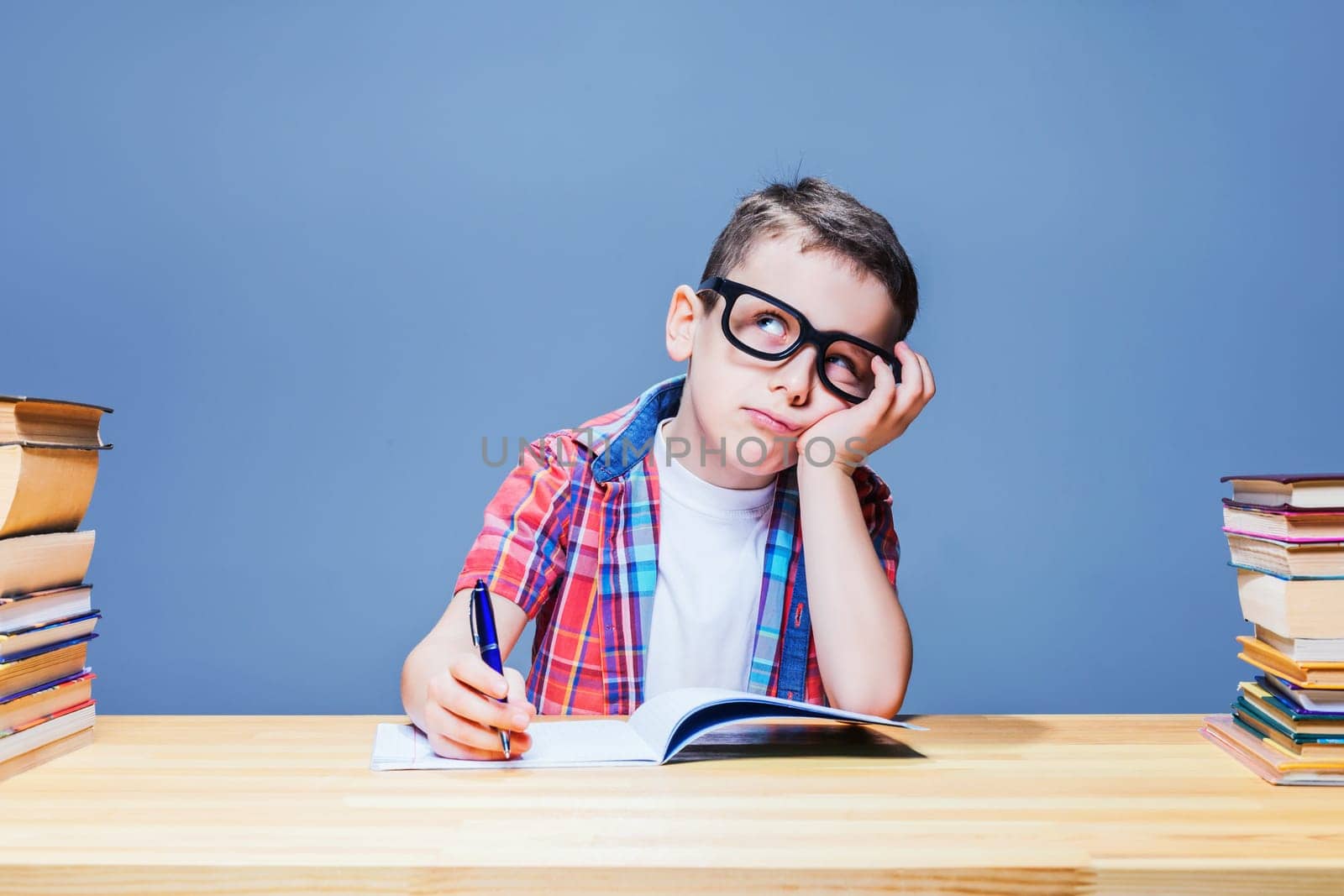 Little schoolboy learns homework at the desk in classroom. Pupil in glasses gets knowledge