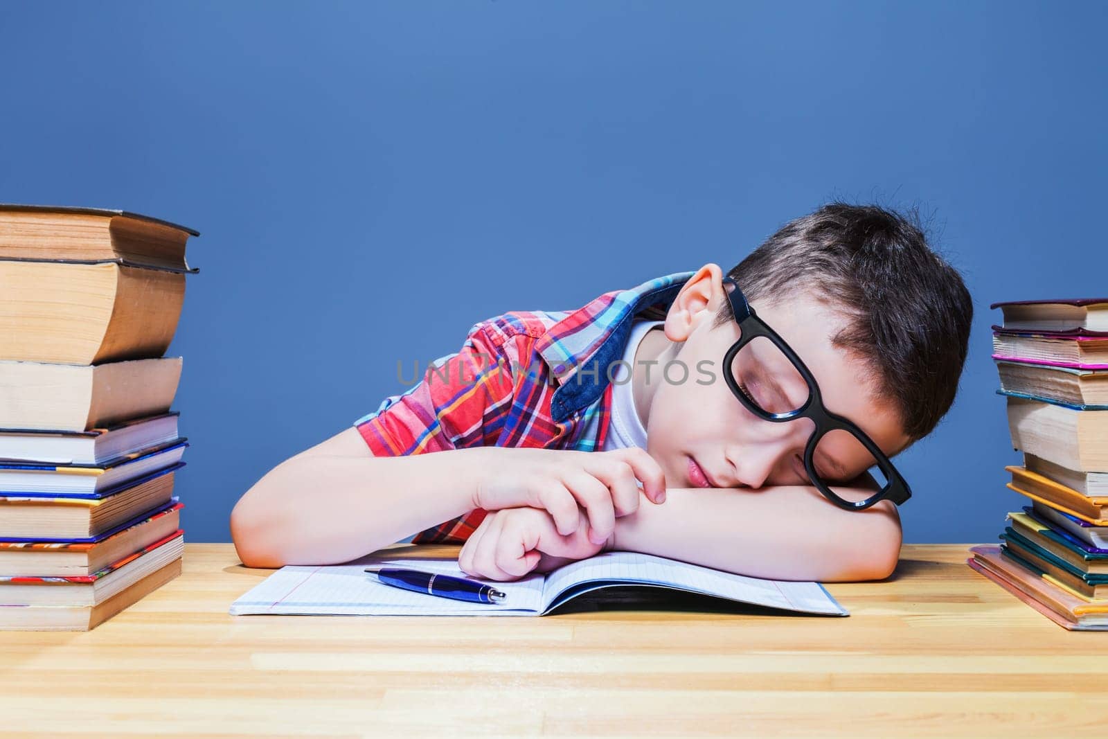Cute child asleep at the desk in school library. Pupil in glasses against many books