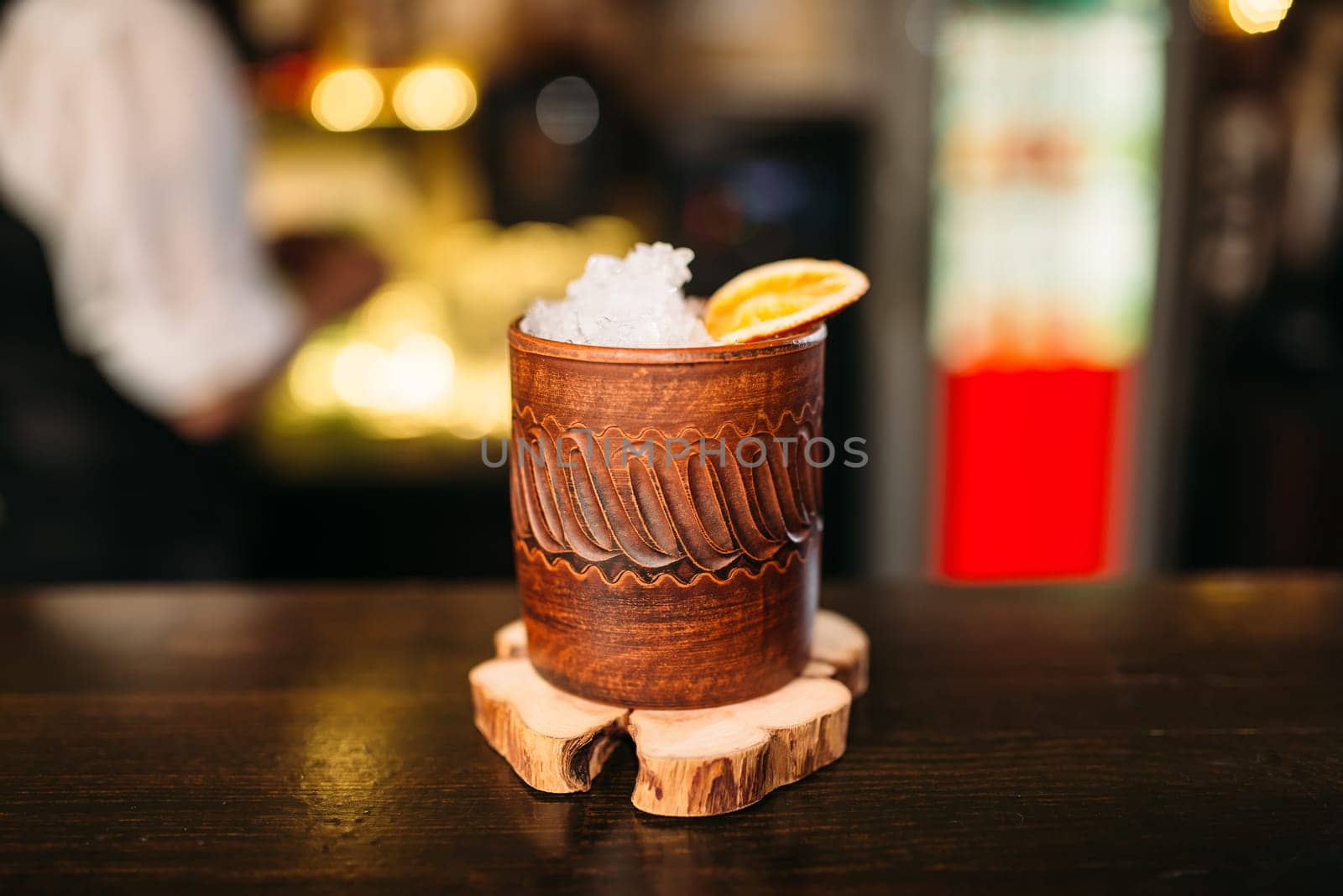 Alcoholic beverage with lemon and ice in wooden cup closeup.