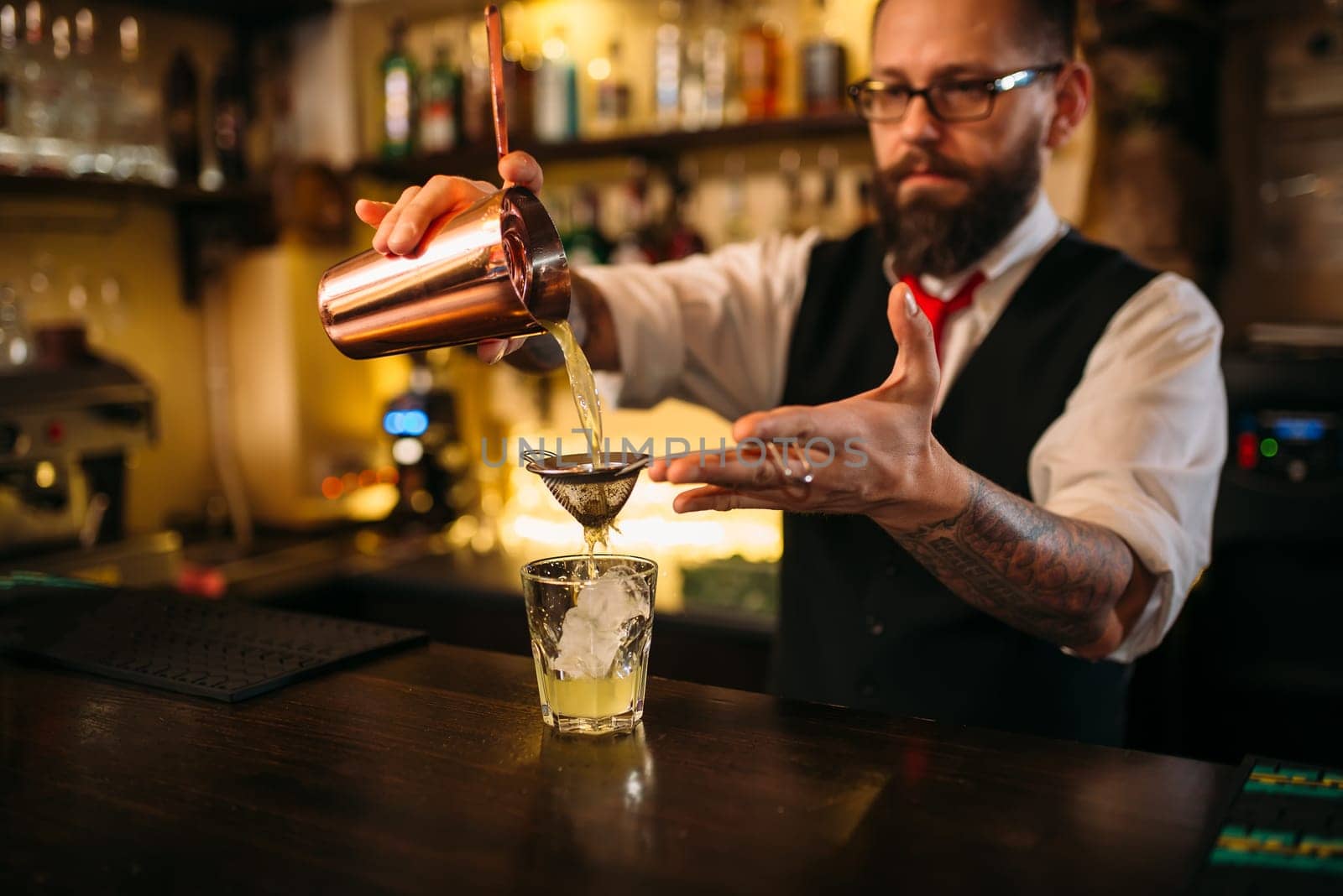 Barman flaring behind bar counter. Restaurant shelves with alcoholic drinks bottles on background