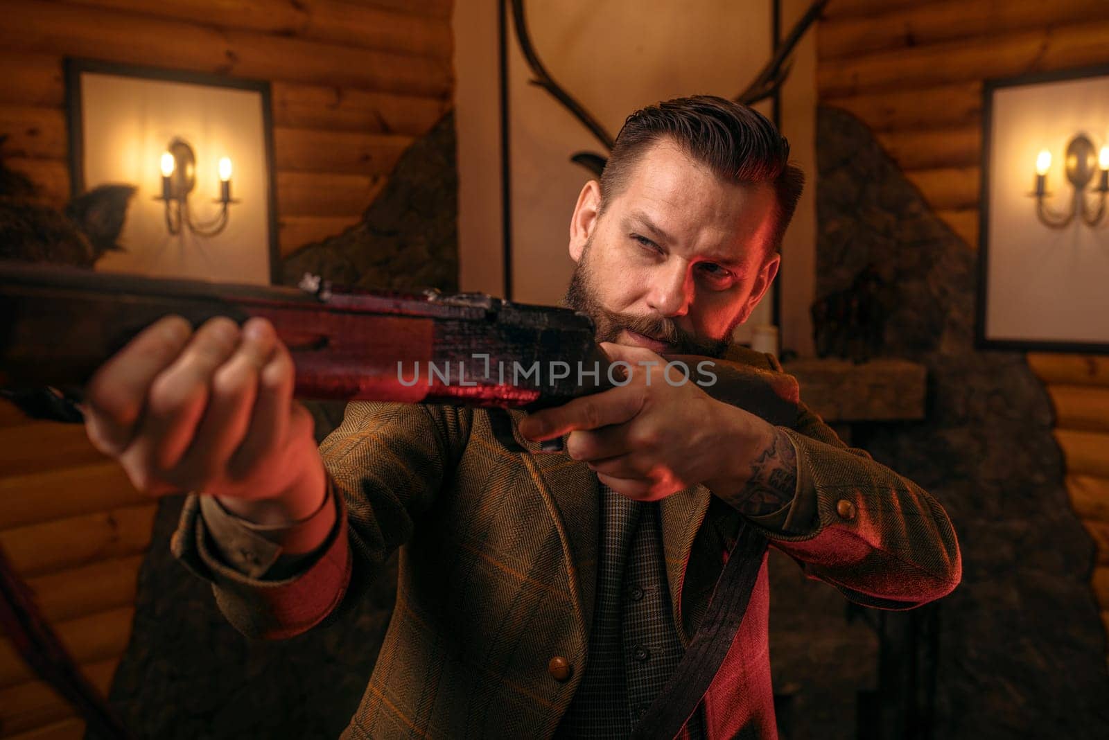 Hunter man aims of the antique hunting rifle. Fireplace, stuffed wild animals, bear skin and other trophies on background