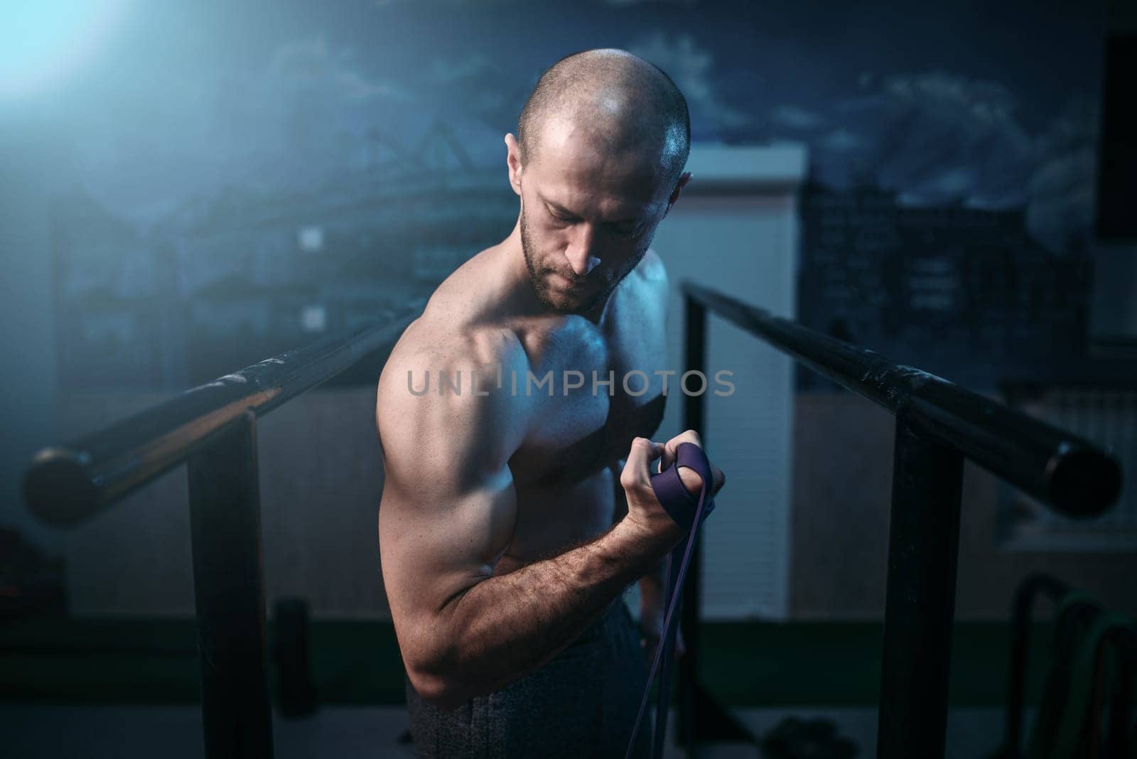 Muscular sports man exercises with elastic rubber band. Active sport lifestyle. Male strong biceps