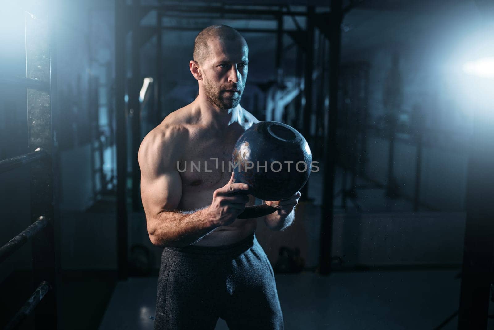 Strong weightlifter workout with kettlebell in gym. Man with muscular torso training with weight