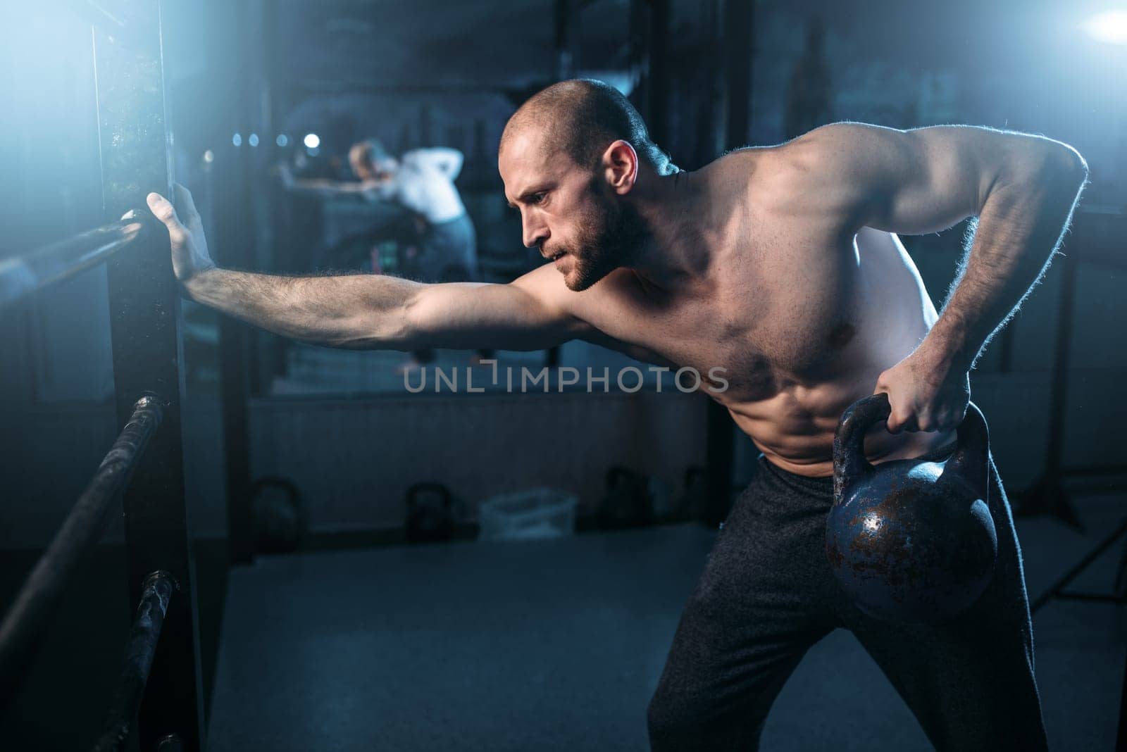 Muscular athlete workout, man lifting kettlebell. Strong sportsman training with weight