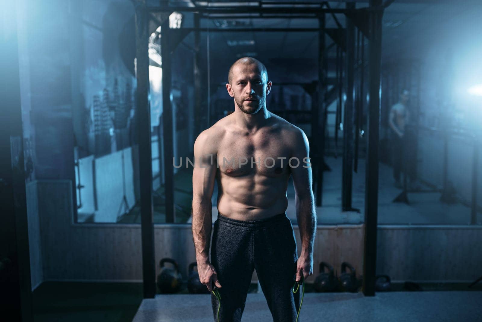 Portrait of strong athlete with jump rope in hands on workout. Sportsman on fitness training in gym. Active sport lifestyle
