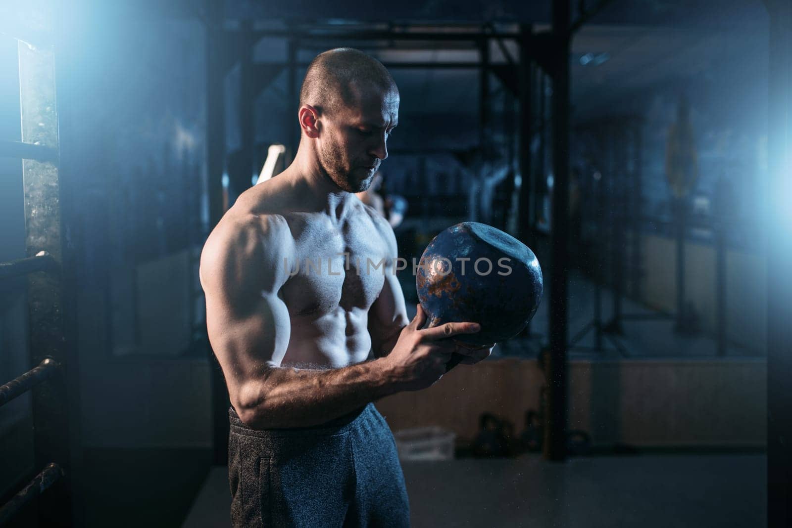 Strong weightlifter workout with kettlebell in gym. Man with muscular torso training with weight