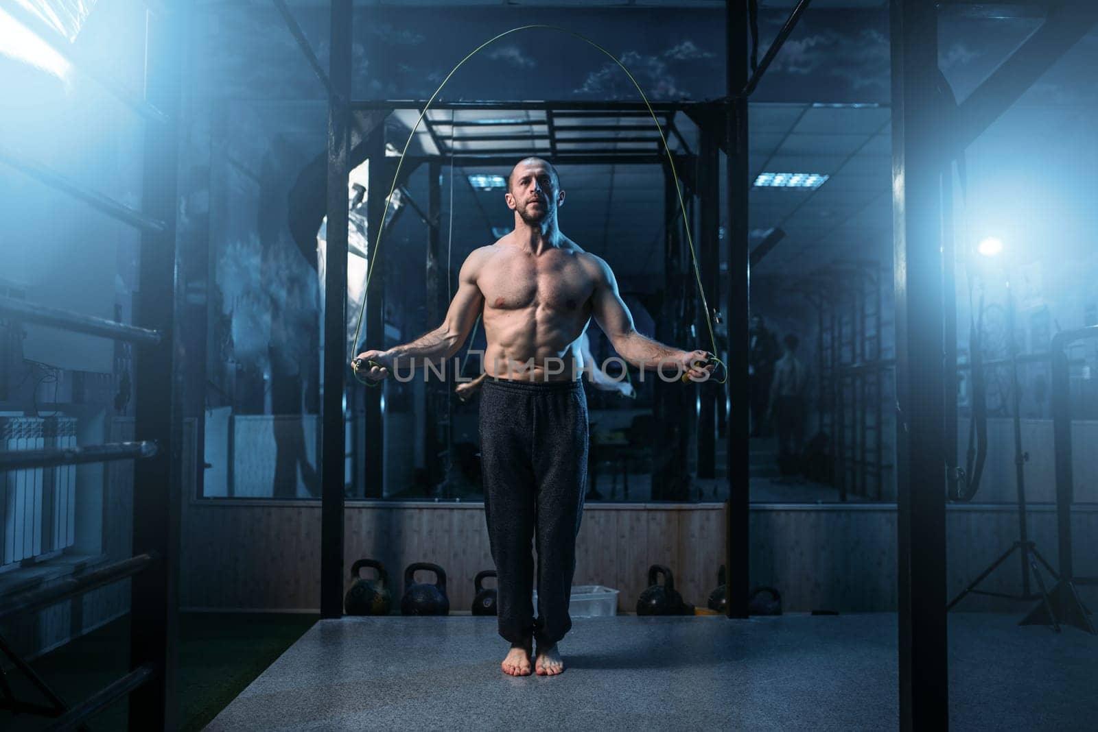 Muscular athlete exercises with jump rope in gym. Sportsman on fitness training. Active sport lifestyle