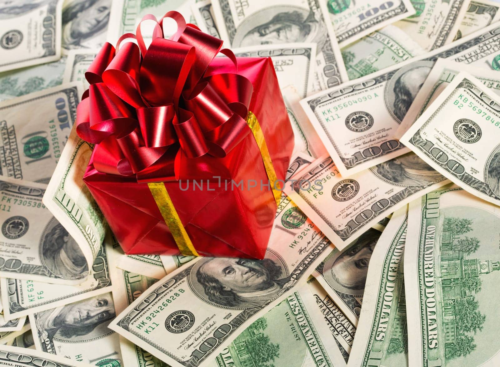 Red gift box on heap of $100 dollar bills