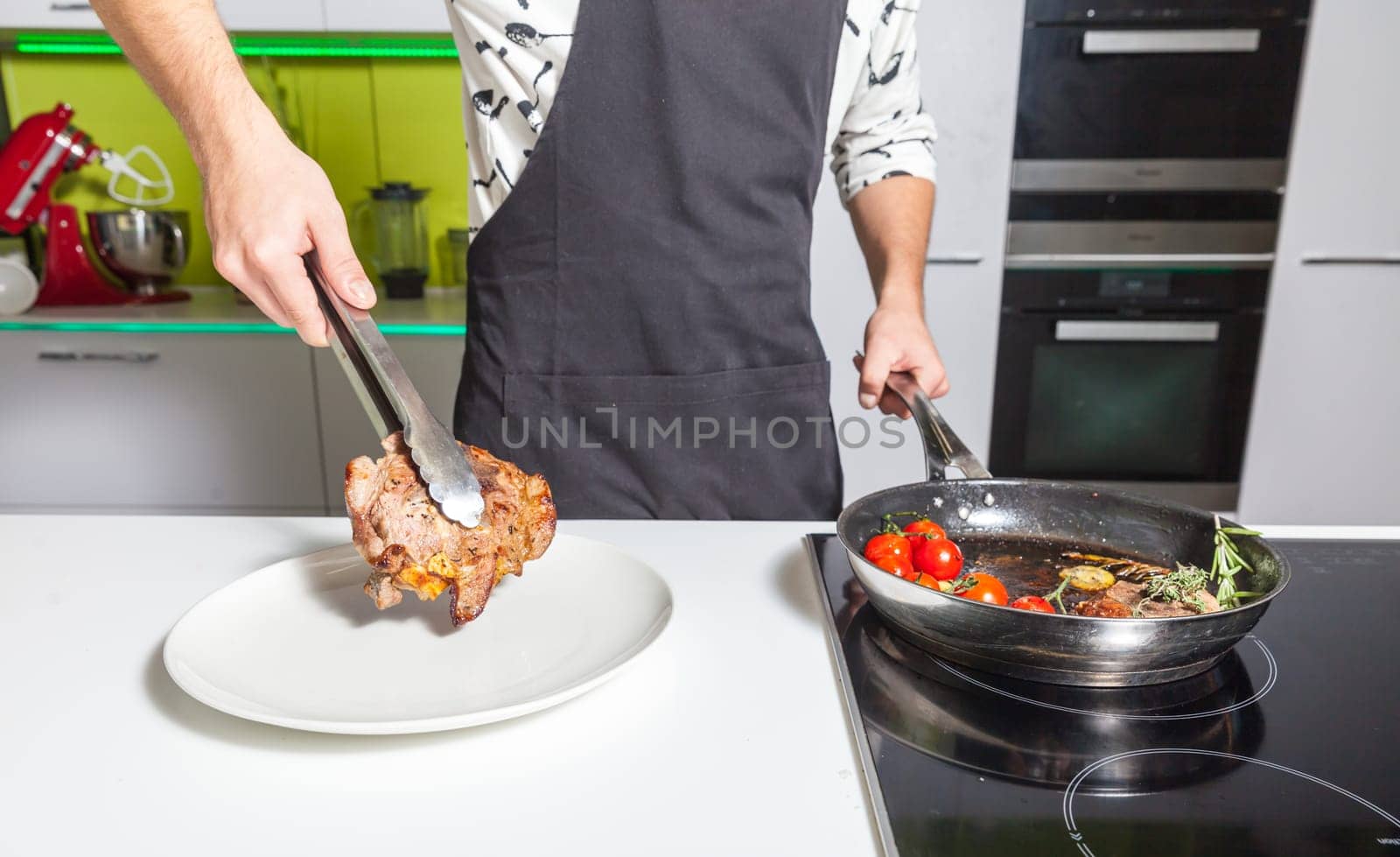 Young man putting fried meat to the plate at home kitchen