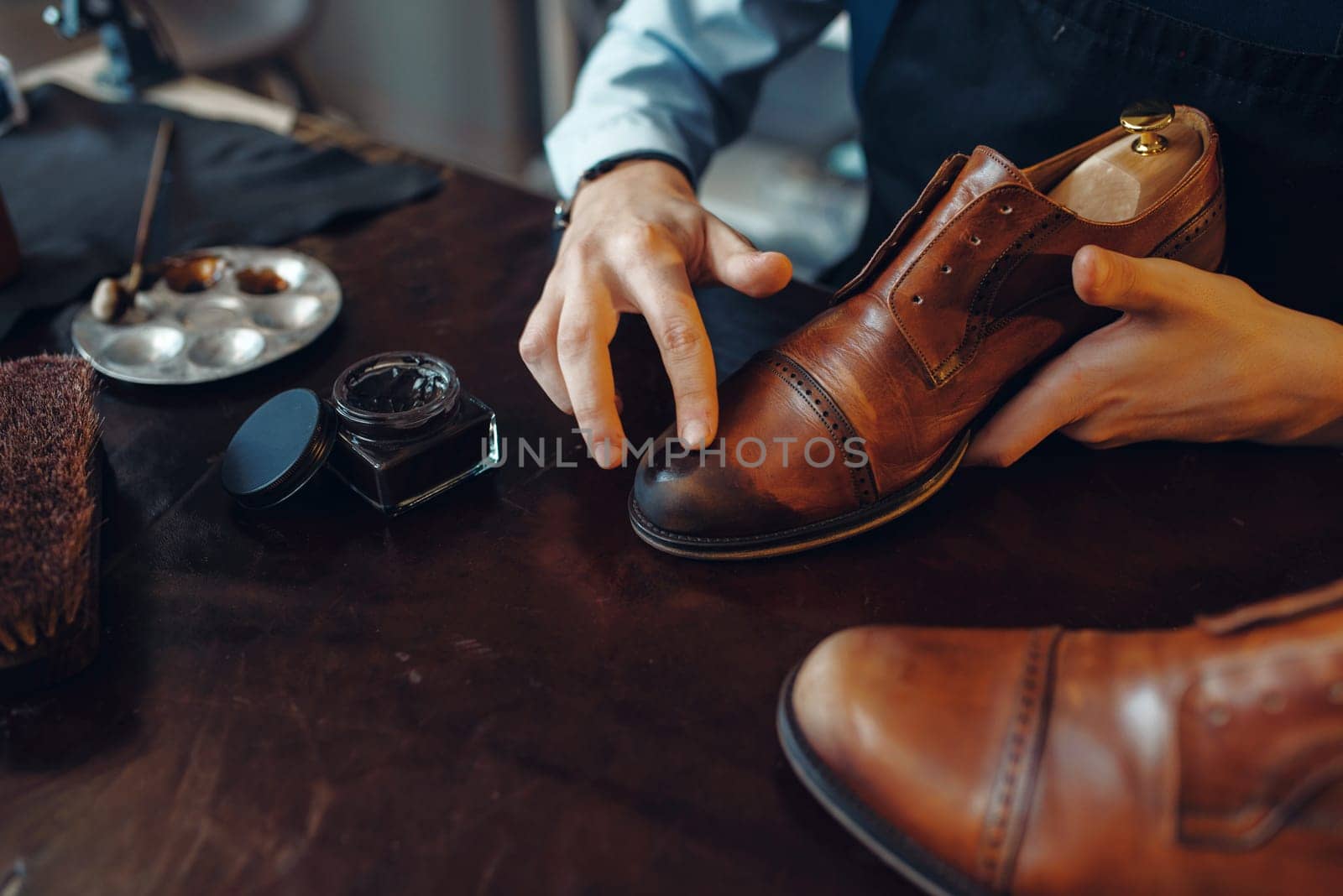 Shoemaker applies black shoe polish, footwear repair service. Craftsman skill, shoemaking workshop, master works with boots, cobbler shop