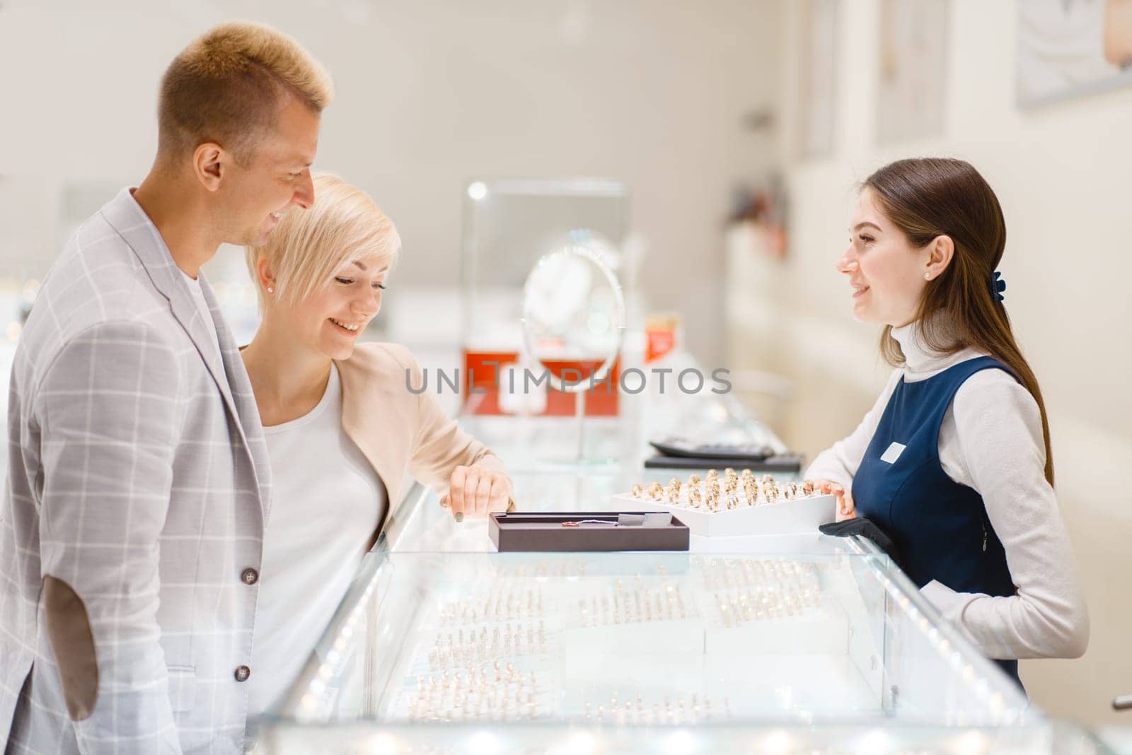 Happy love couple buying gold decoration. Male and female consumers looking on jewels in jewelry store. Man and woman choosing wedding rings. Future bride and groom in jewellery shop