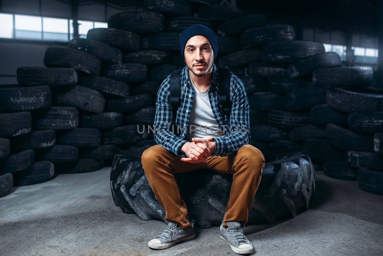 Stalker, alone traveler against mountain of tires, abandoned factory. Danger zone, deserted place
