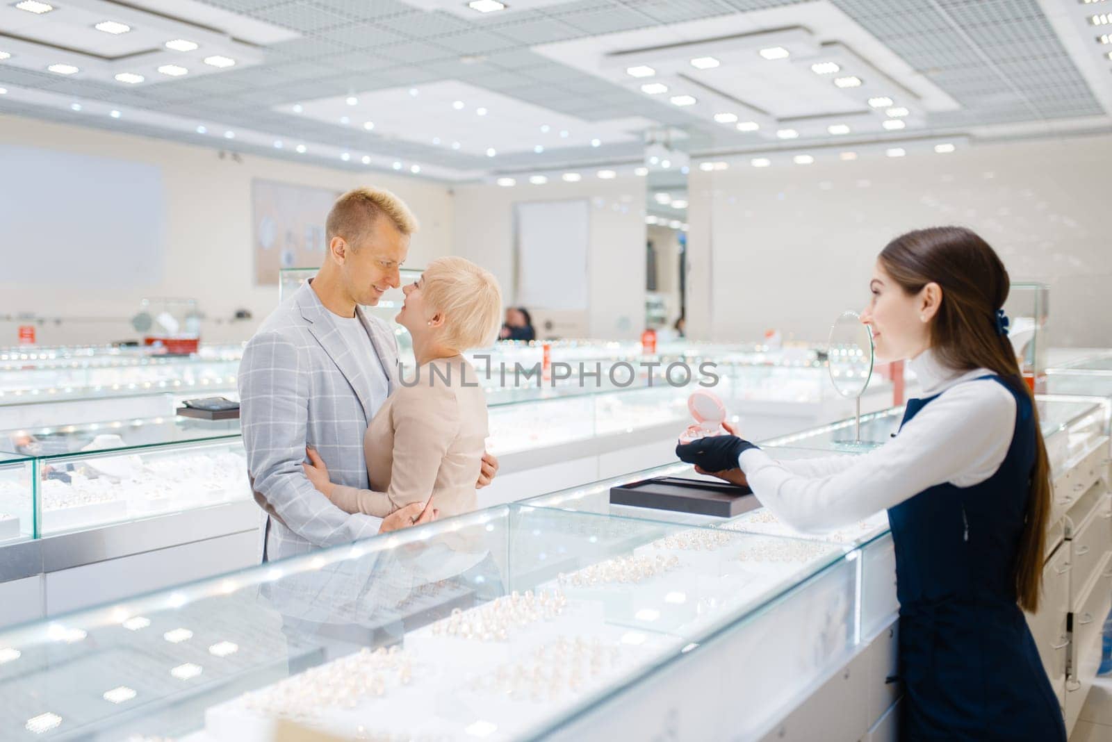 Happy love couple buying gold decoration. Male and female consumers looking on jewels in jewelry store. Man and woman choosing wedding rings. Future bride and groom in jewellery shop
