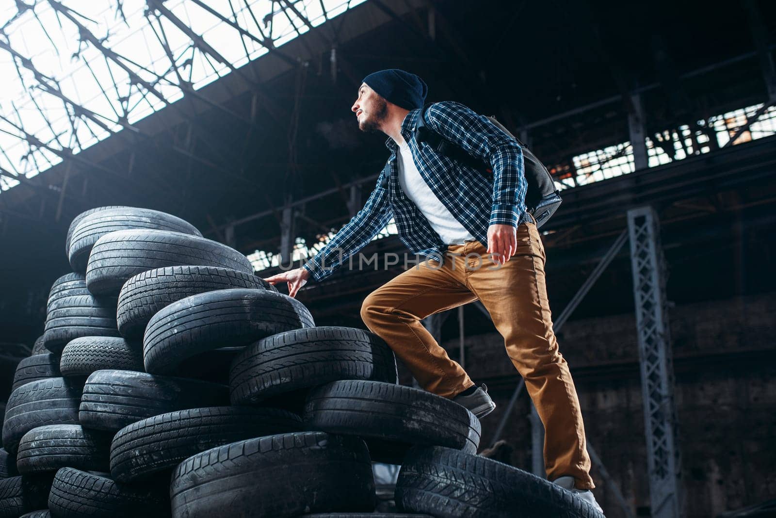 Stalker, traveler climbs a mountain of tires, abandoned factory. Danger zone, deserted place