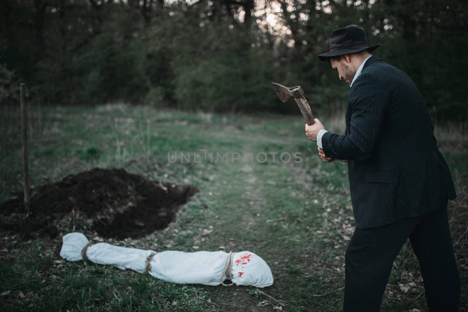 Maniac with an axe against victim body wrapped in a canvas, serial murderer concept, crime horror