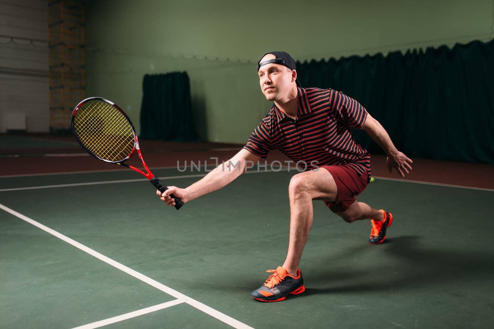 Man with tennis racket playing on indoor court. Sport training of male tennis player