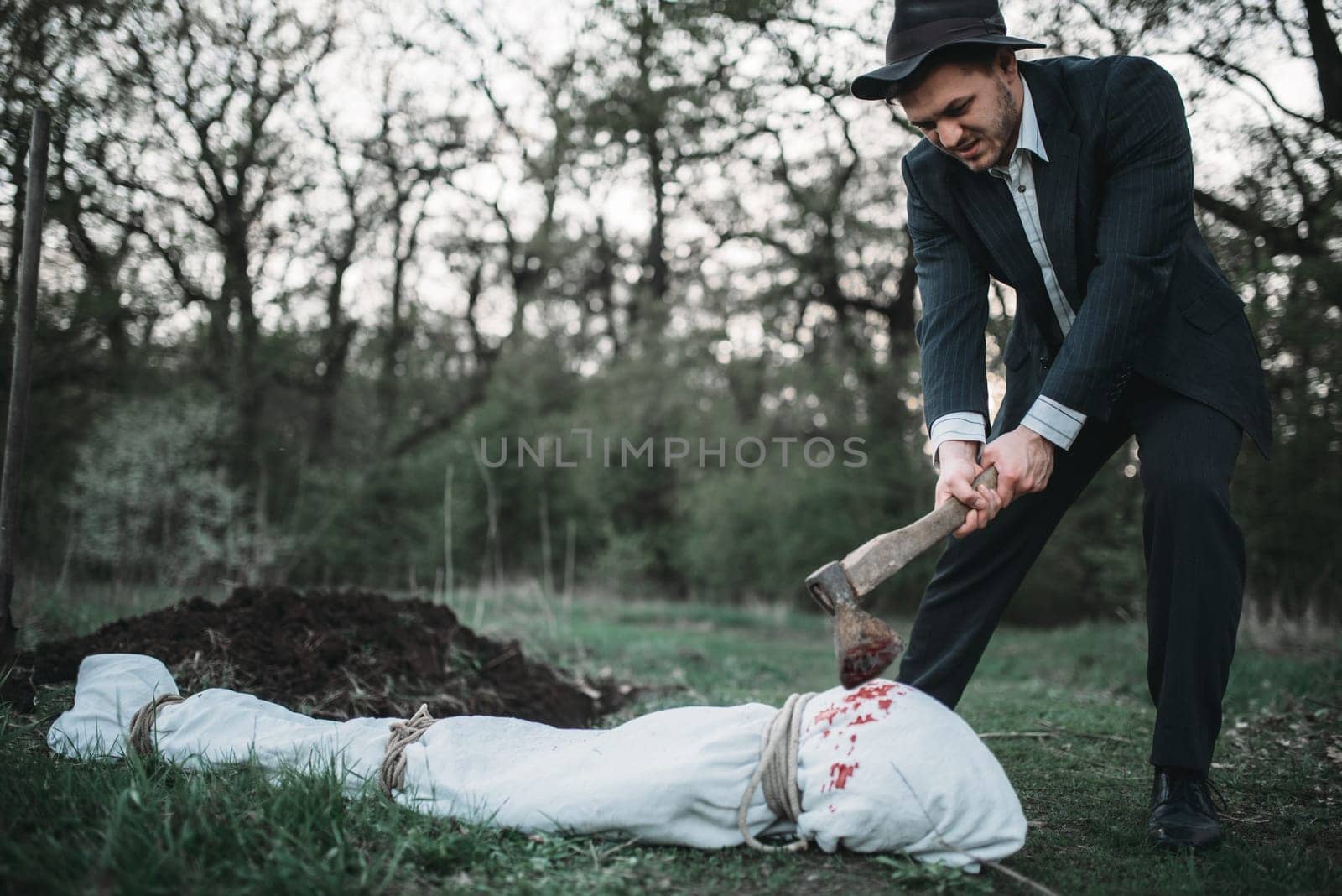 Maniac with an axe against victim body wrapped in a canvas, serial murderer concept, crime horror