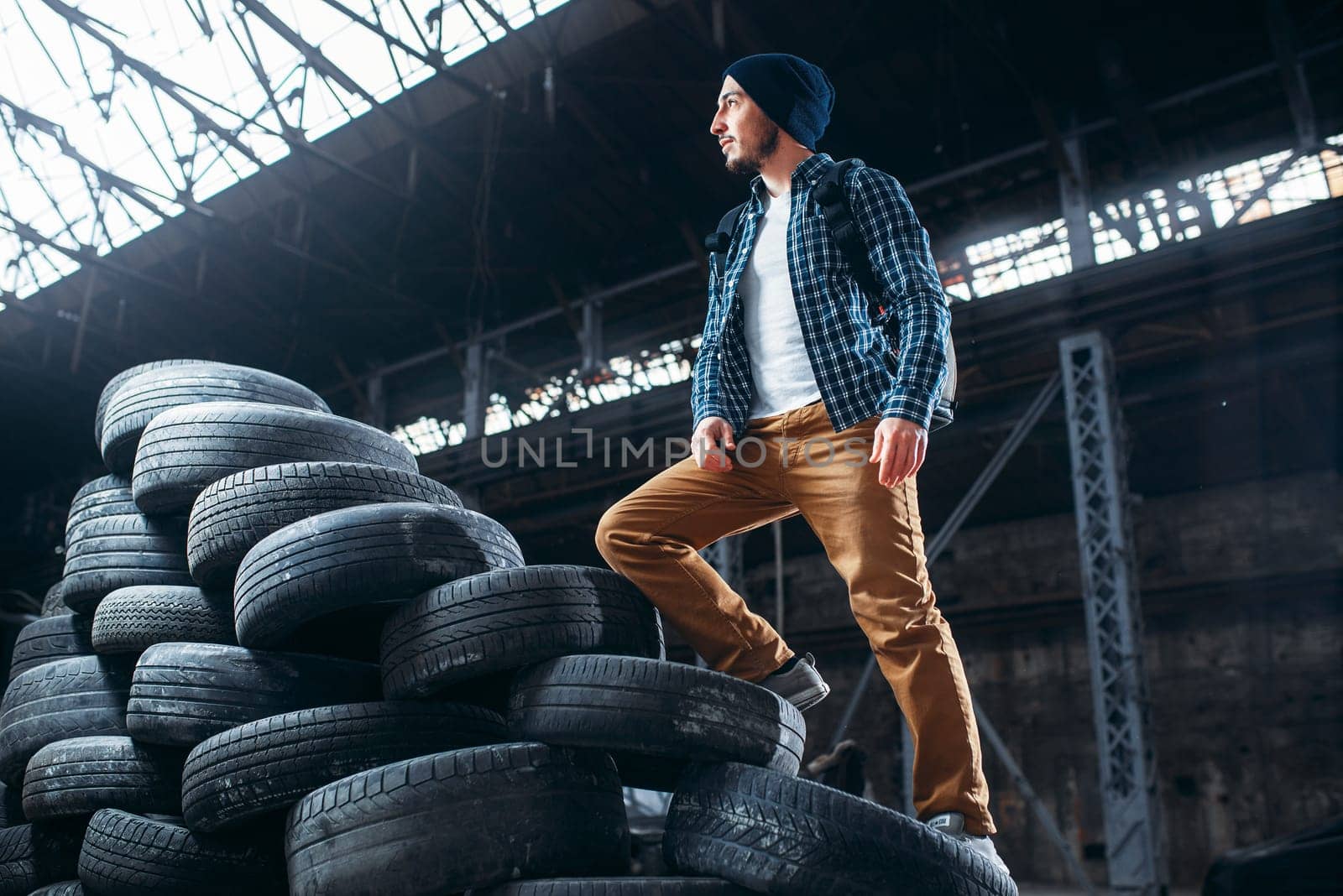 Stalker, traveler climbs a mountain of tires, abandoned factory. Danger zone