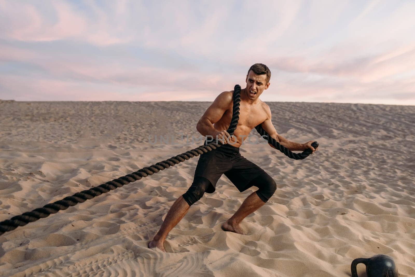 Muscular man doing exercise with rope in desert at sunny day. Strong motivation in sport, strength outdoor training