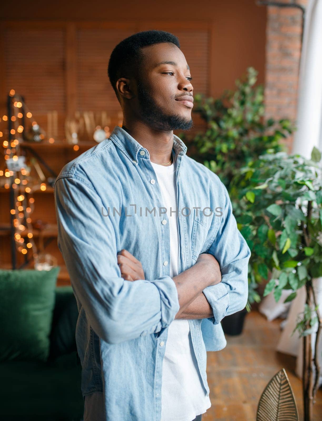Black man with a cunning look in the living room, relaxation at home. Young african american male person standing in his house