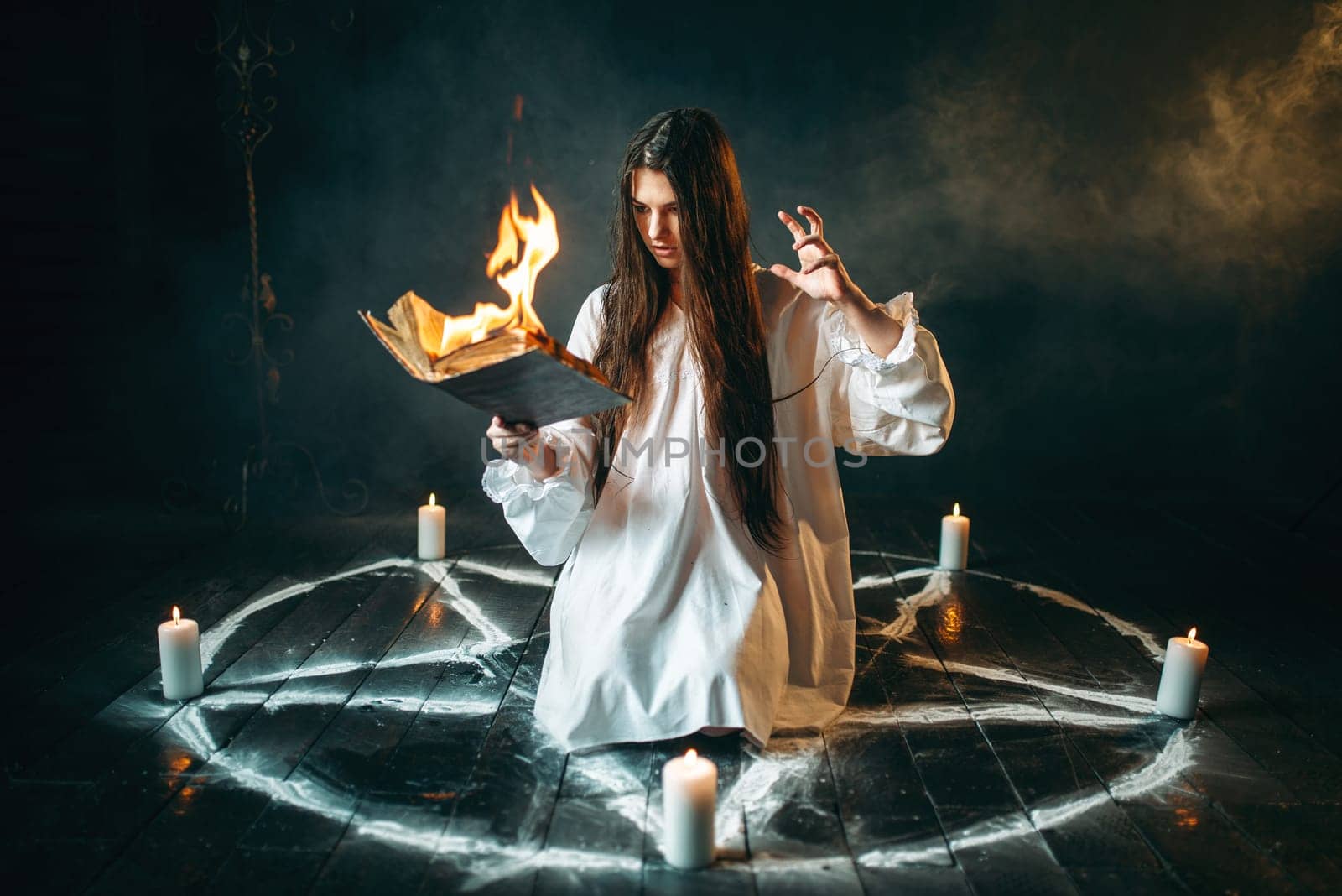Young woman in white shirt sitting in the center of burning pentagram circle and reads spellbook, gark magic ritual