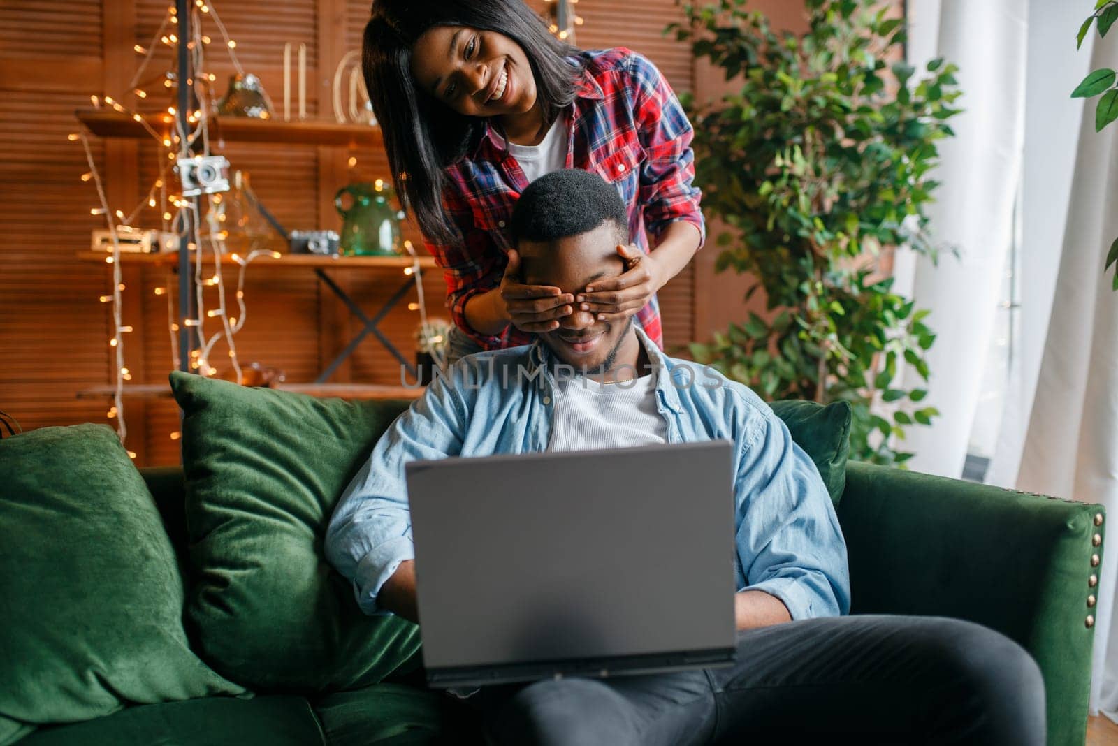 Black couple with laptop having fun on sofa at home. Happy african love couple leisures in their house, cheerful family relaxing in living room