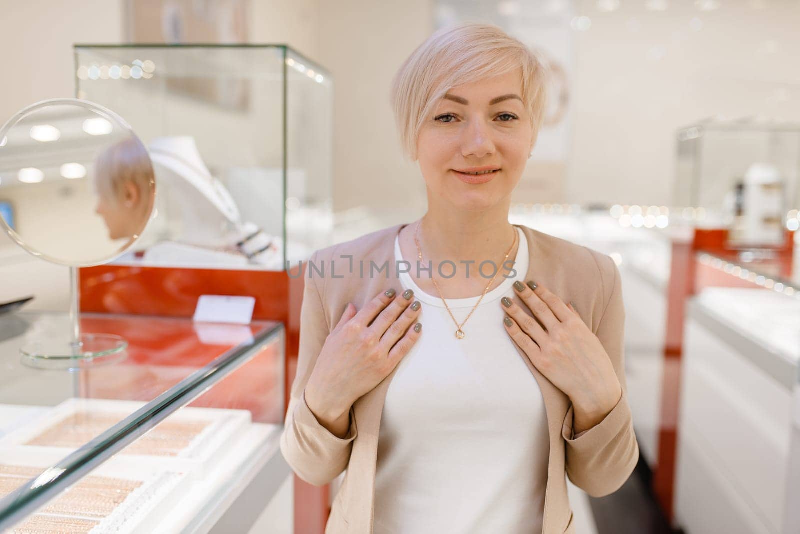 Woman trying on golden necklace at the showcase in jewelry store. Female person buying gold decoration in jewellery shop