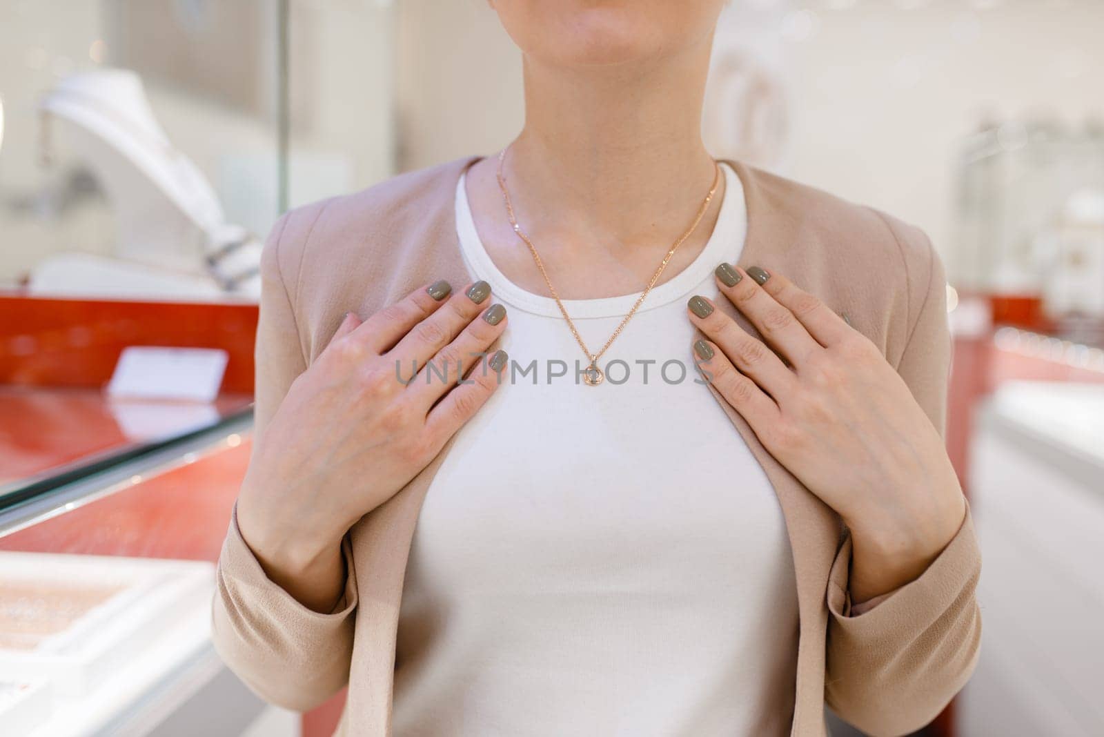 Woman trying on golden necklace at the showcase in jewelry store. Female person buying gold decoration in jewellery shop