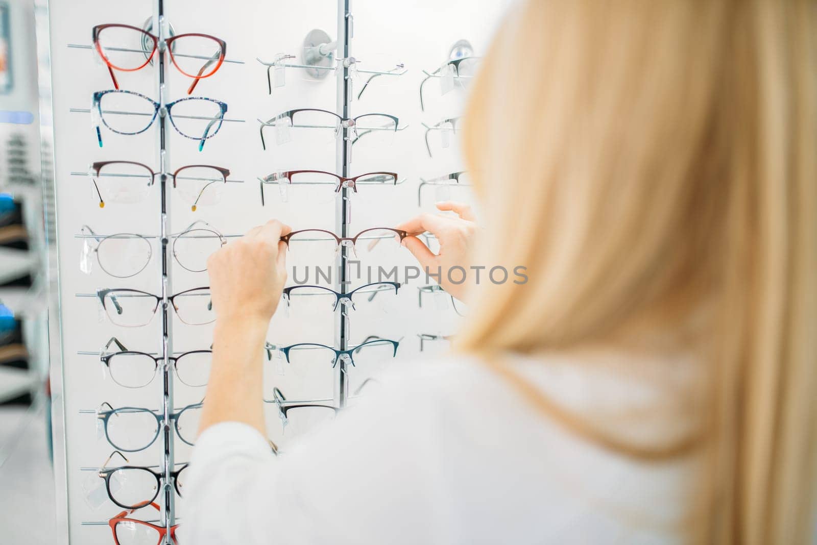 Female optometrist shows glasses in optics store. Selection of eyeglasses with professional optician