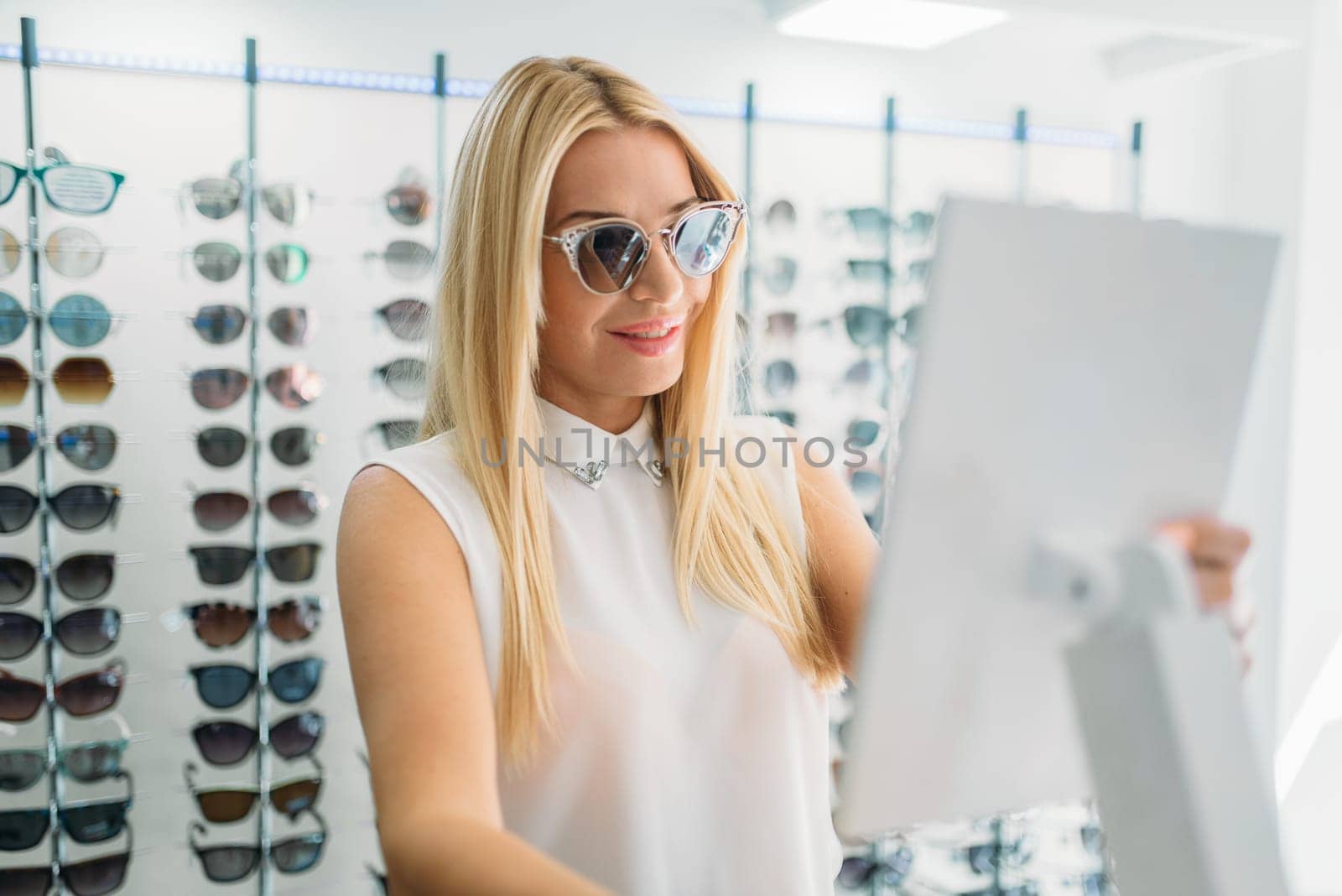 Female customer shooses sunglasses in optics store. Selection of eyes protection in glasses shop, optometry concept