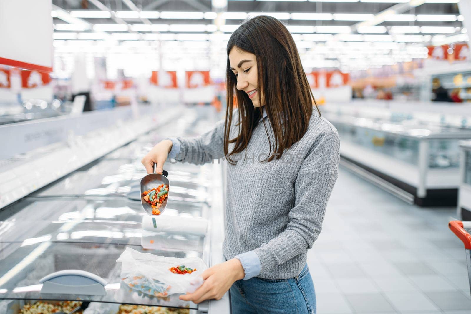 Woman picks up a package of frozen vegetables in a supermarket, family shopping. Female customer buys products in shop, buyer in the market