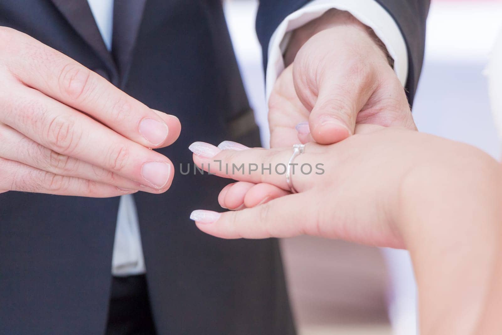 Husband with dark suit and wife with bright dress exchange golden luxury rings. Holding hands and put a ring on each others finger.
