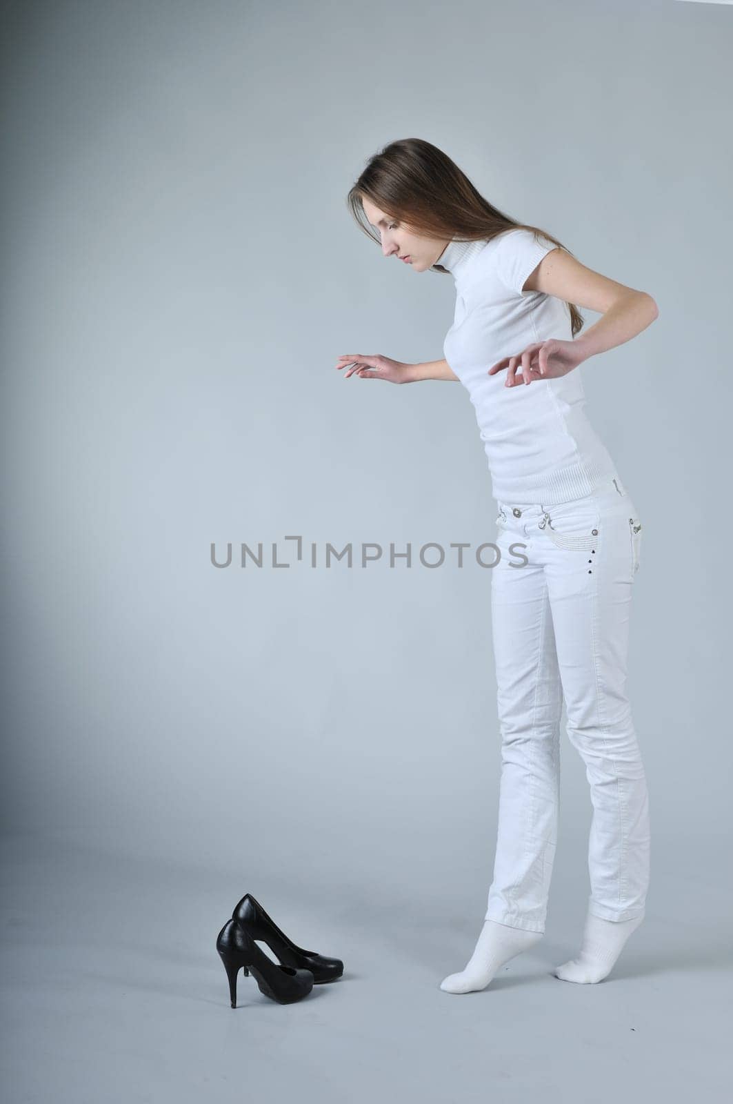Young woman balancing on toes with high heels shoes placed on floor