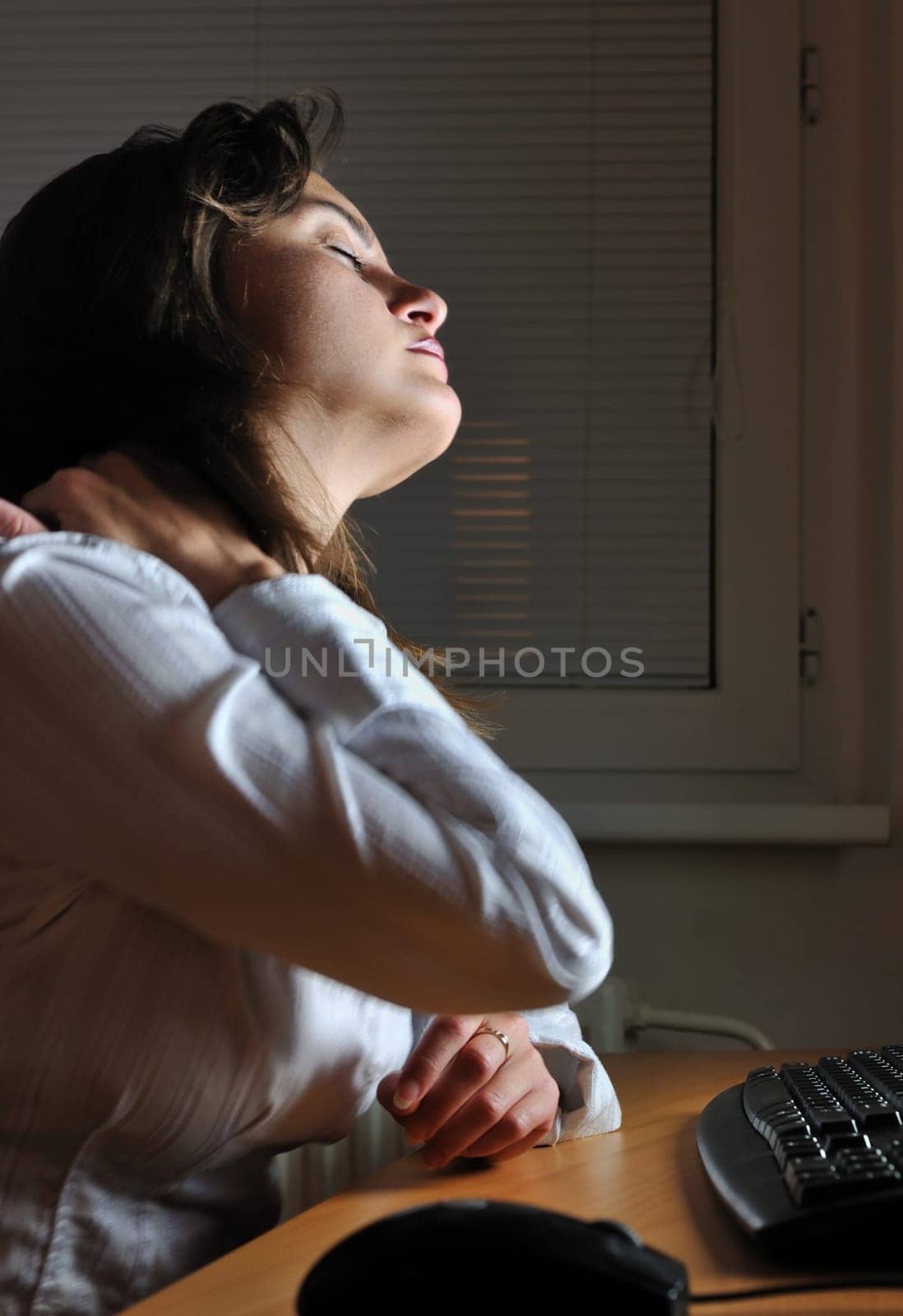 Neck pain - young tired business woman working overtime at computer, night setting