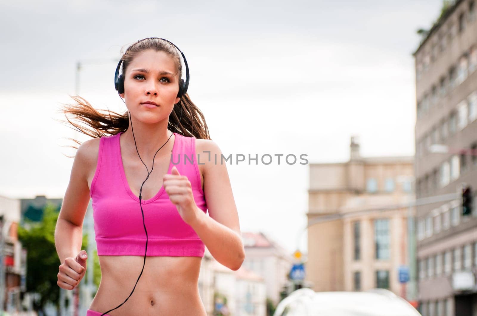 Young beautiful woman with headphones jogging and listening music in street