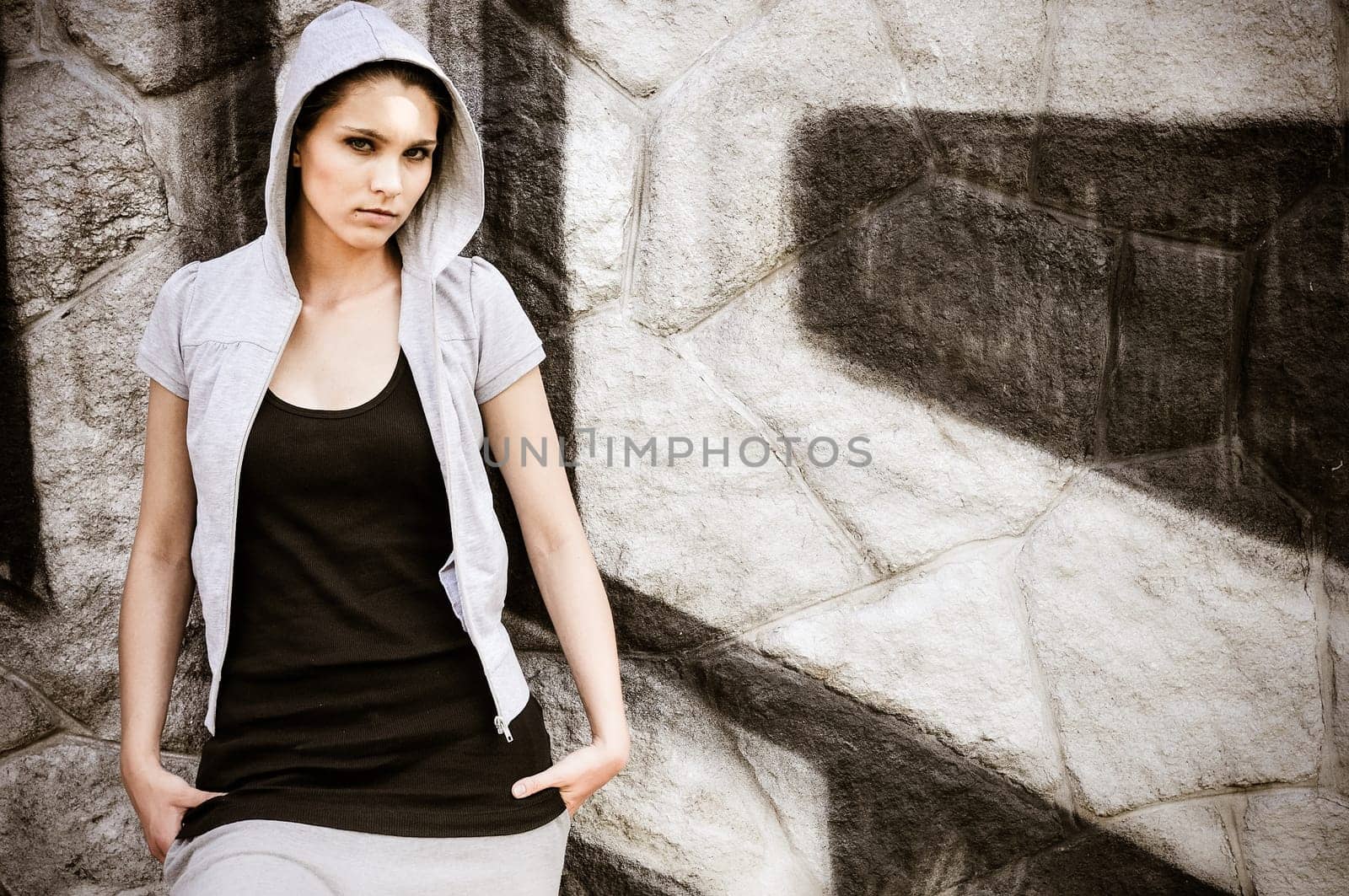 Young person (teenage girl) with hood in hip hop style standing at black and white graffity wall with copy space