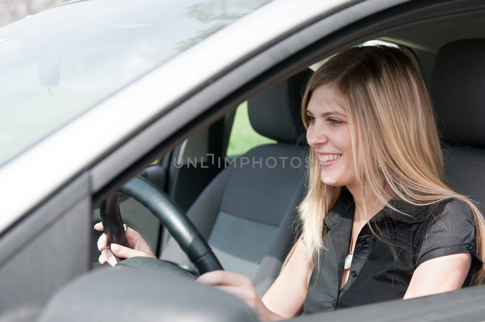 Young beautiful smiling woman driving car - portrait through side window