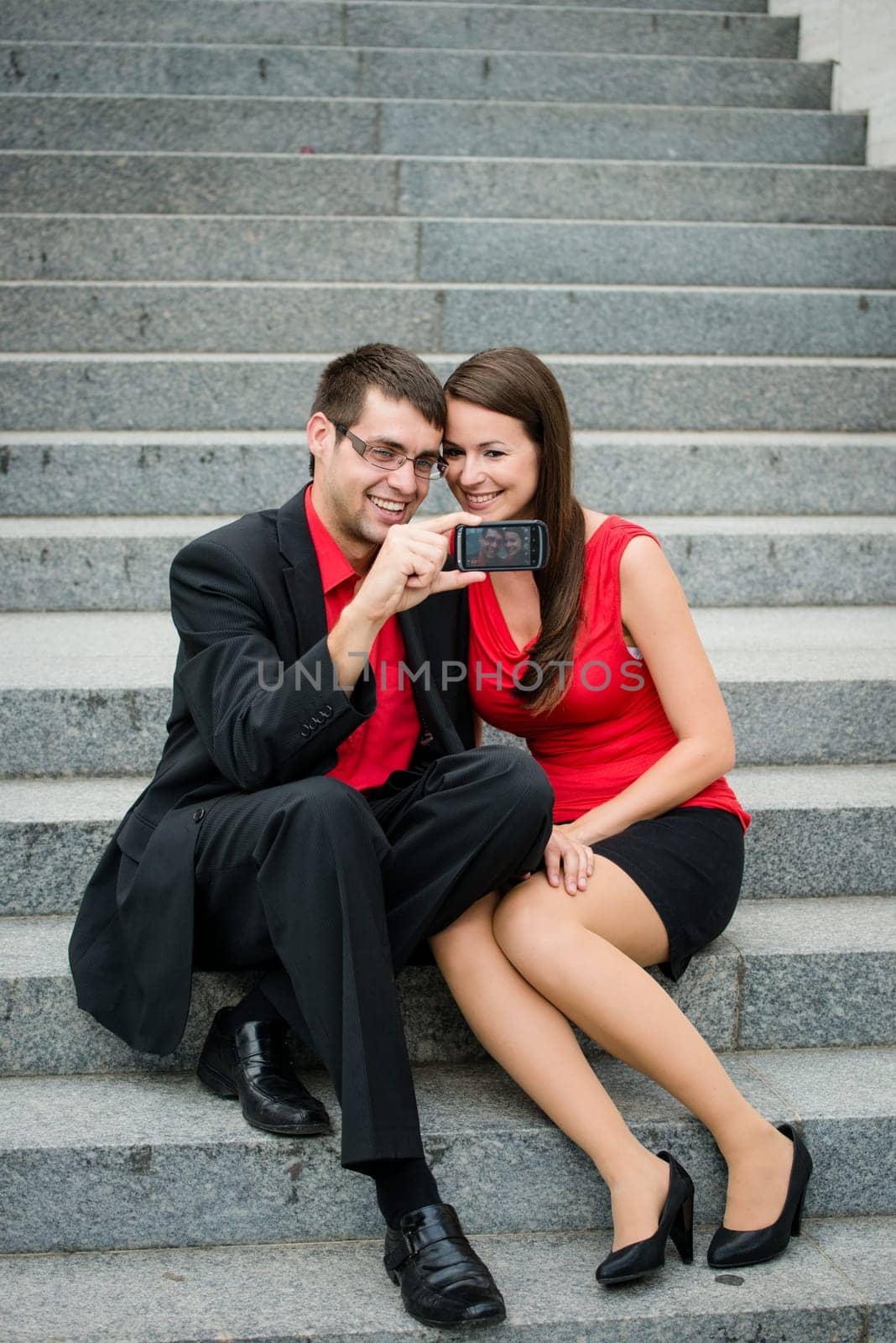 Young couple in business clothes outdoor - man taking photo with smartphone