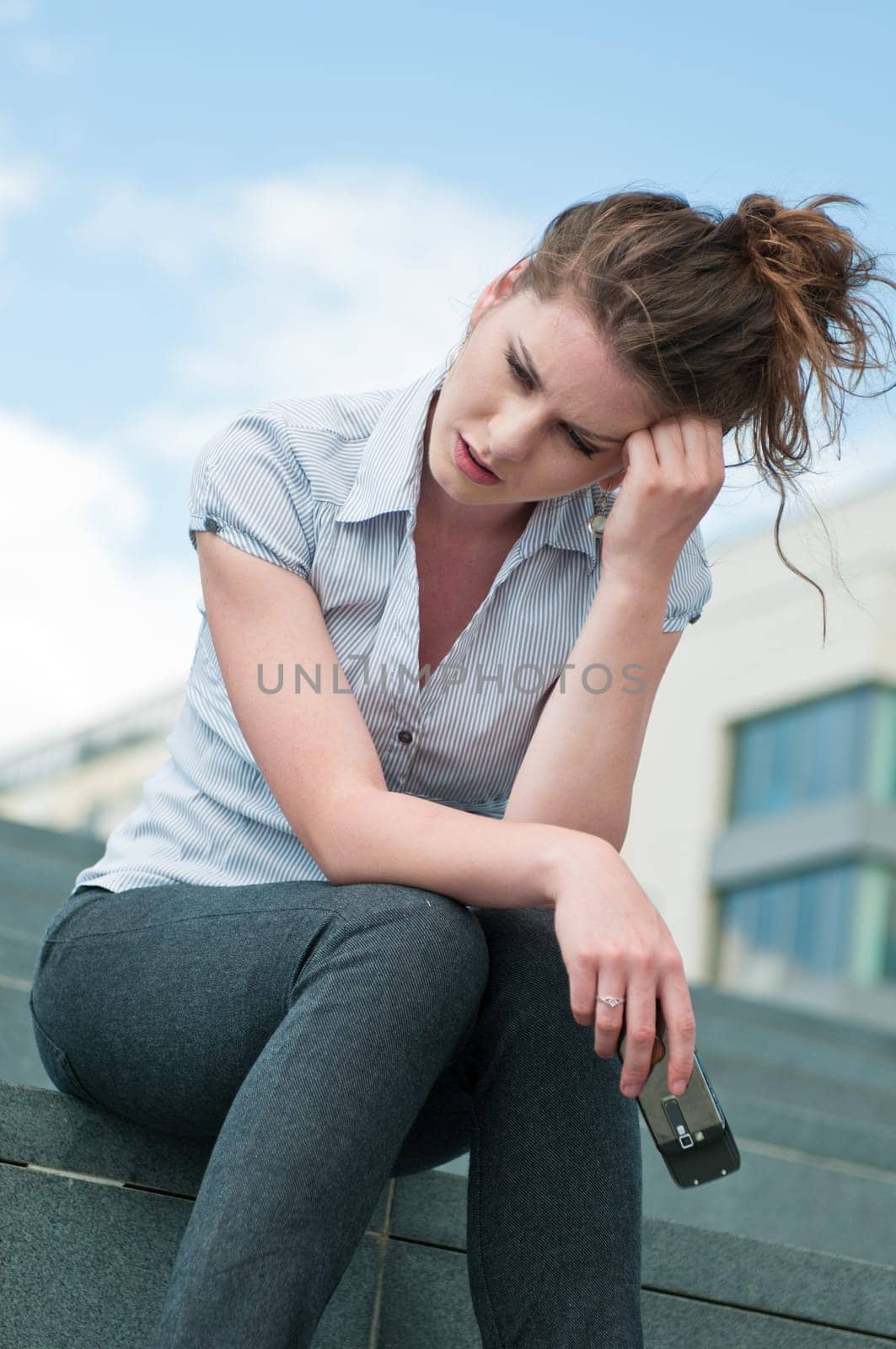 Young worried woman with unhappy expression holding mobile phone - outdoors in urban setting