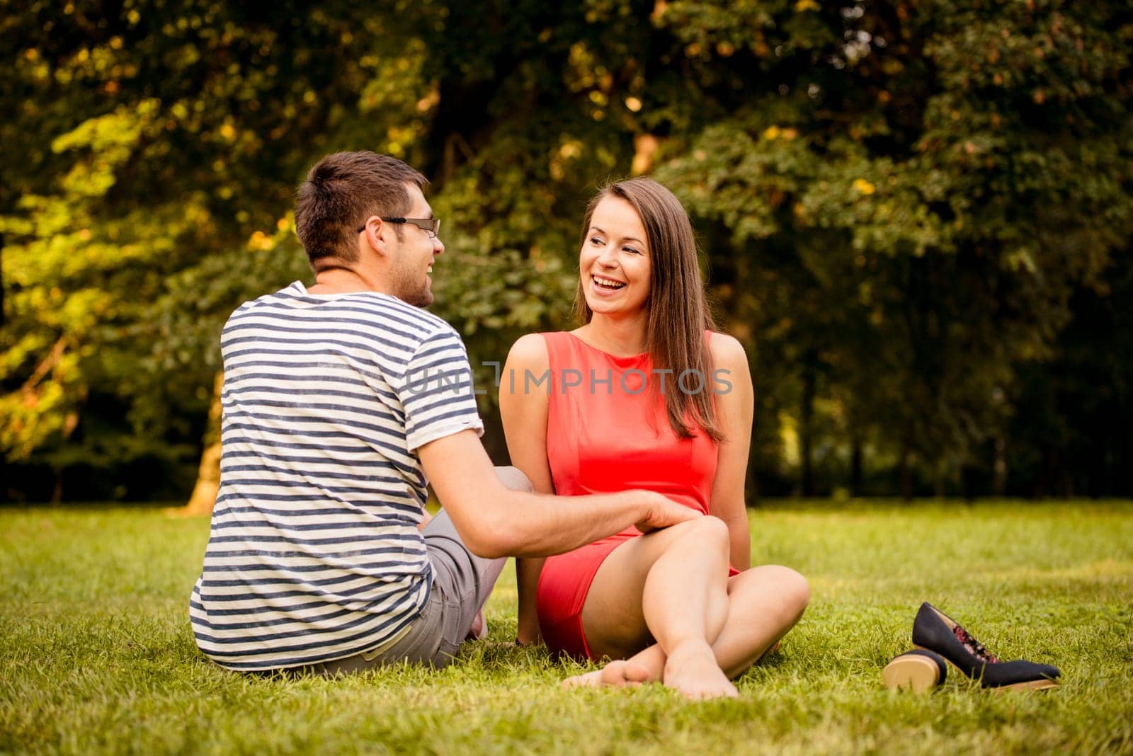 Young smiling couple sitting on grass in park - man has hand on woman knee