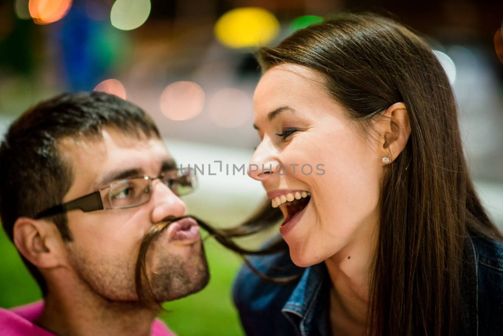 Couple having fun in street at night - man making moustache with his hair