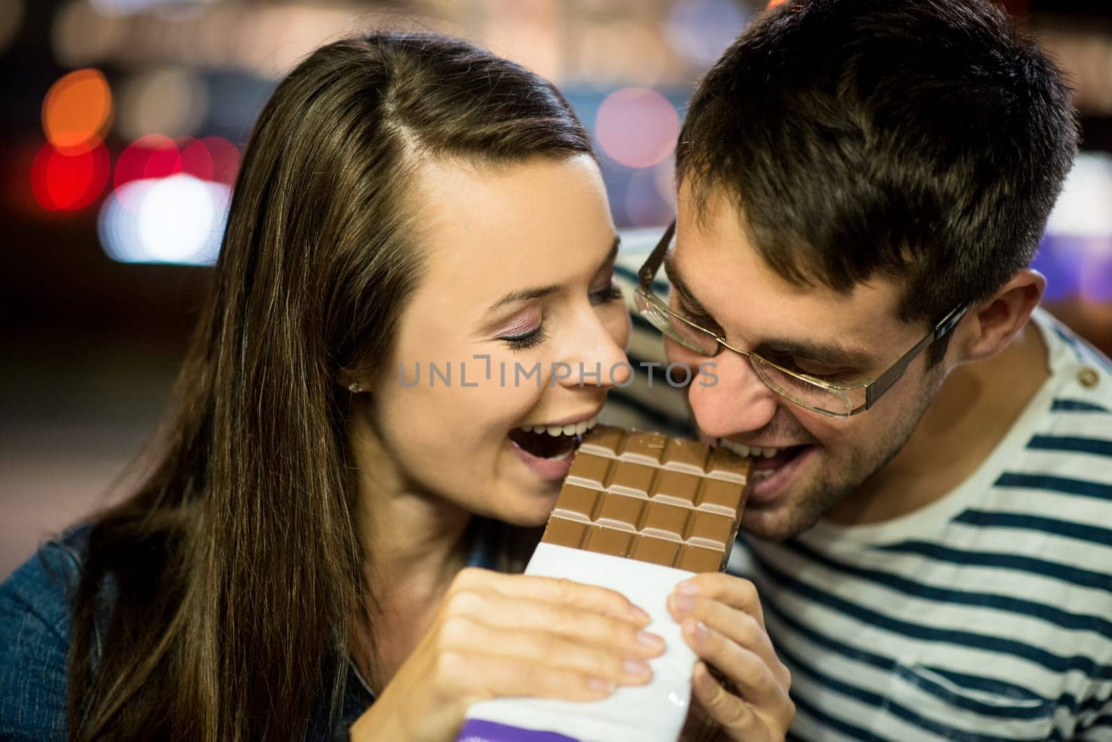 Young couple eat together chocolate on date - in street at night