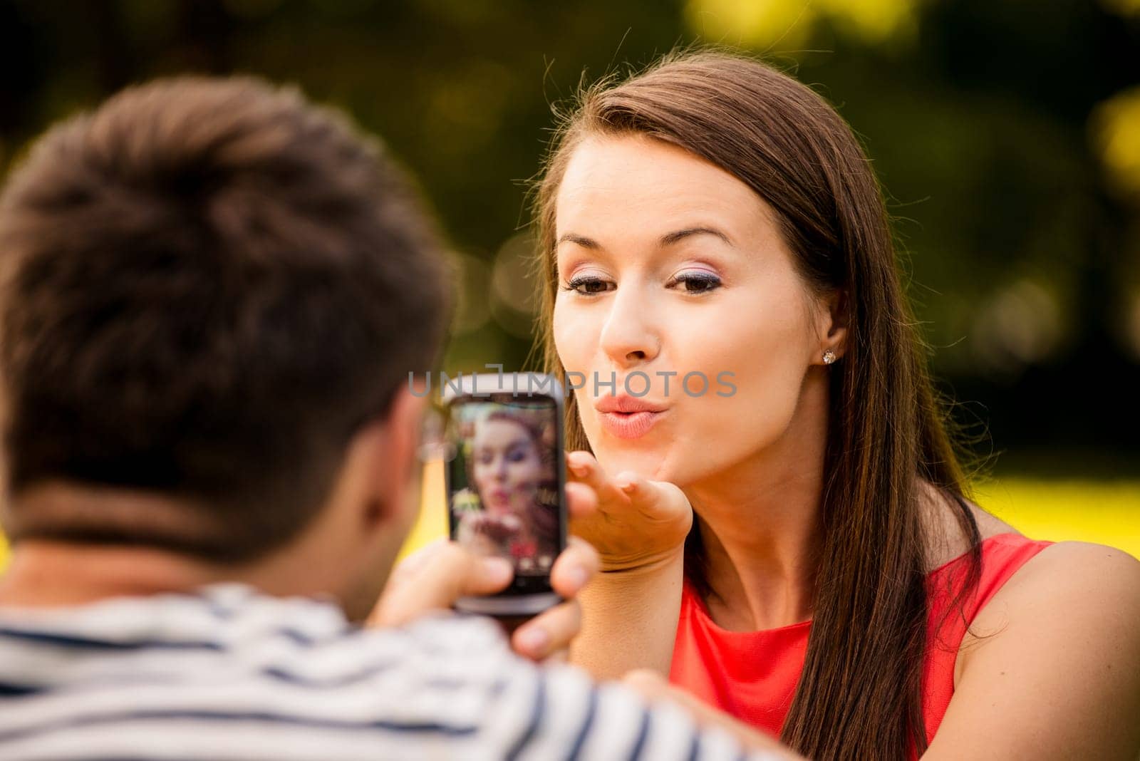 Young man taking photo of her girlfriend with mobile phone in nature