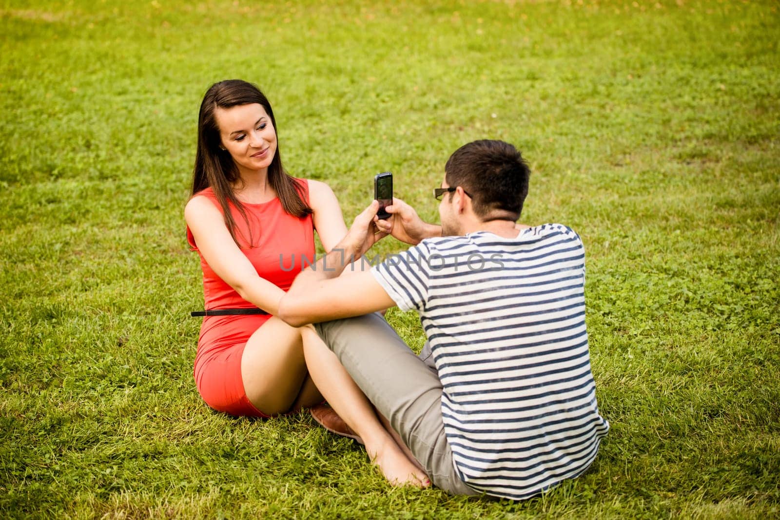Young man taking photo of her girlfriend with mobile phone in nature