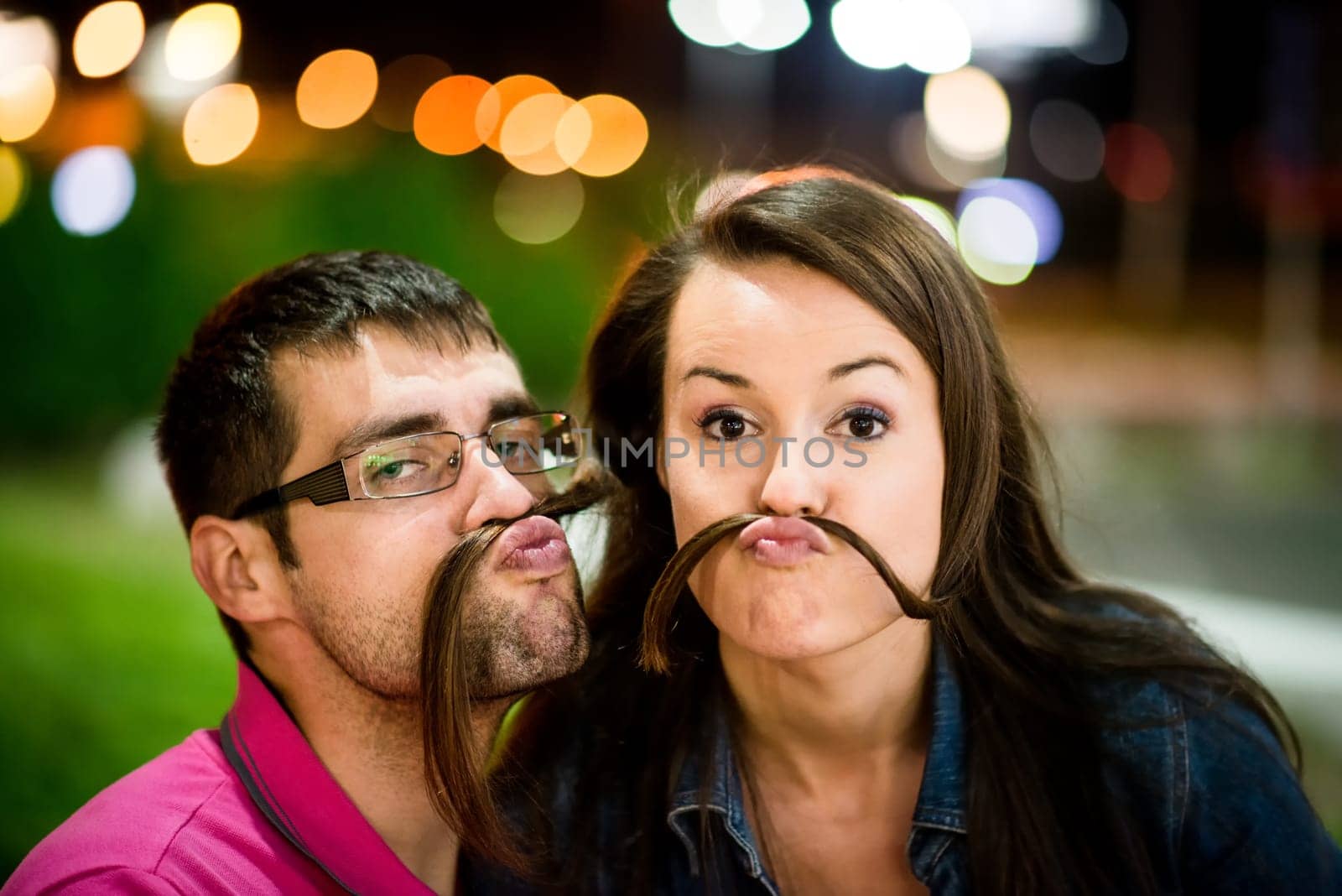 Couple having fun in street at night - making moustache with their hair