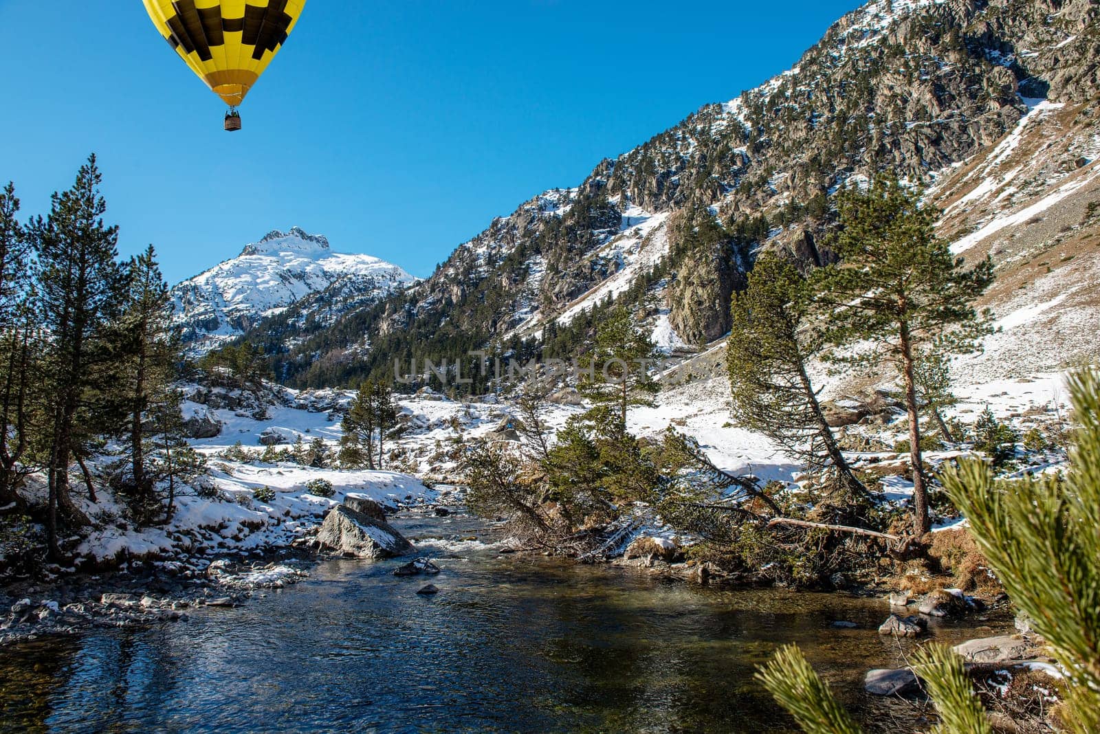 river in the snowy Pyrenees mountains with a yellow hot air balloon