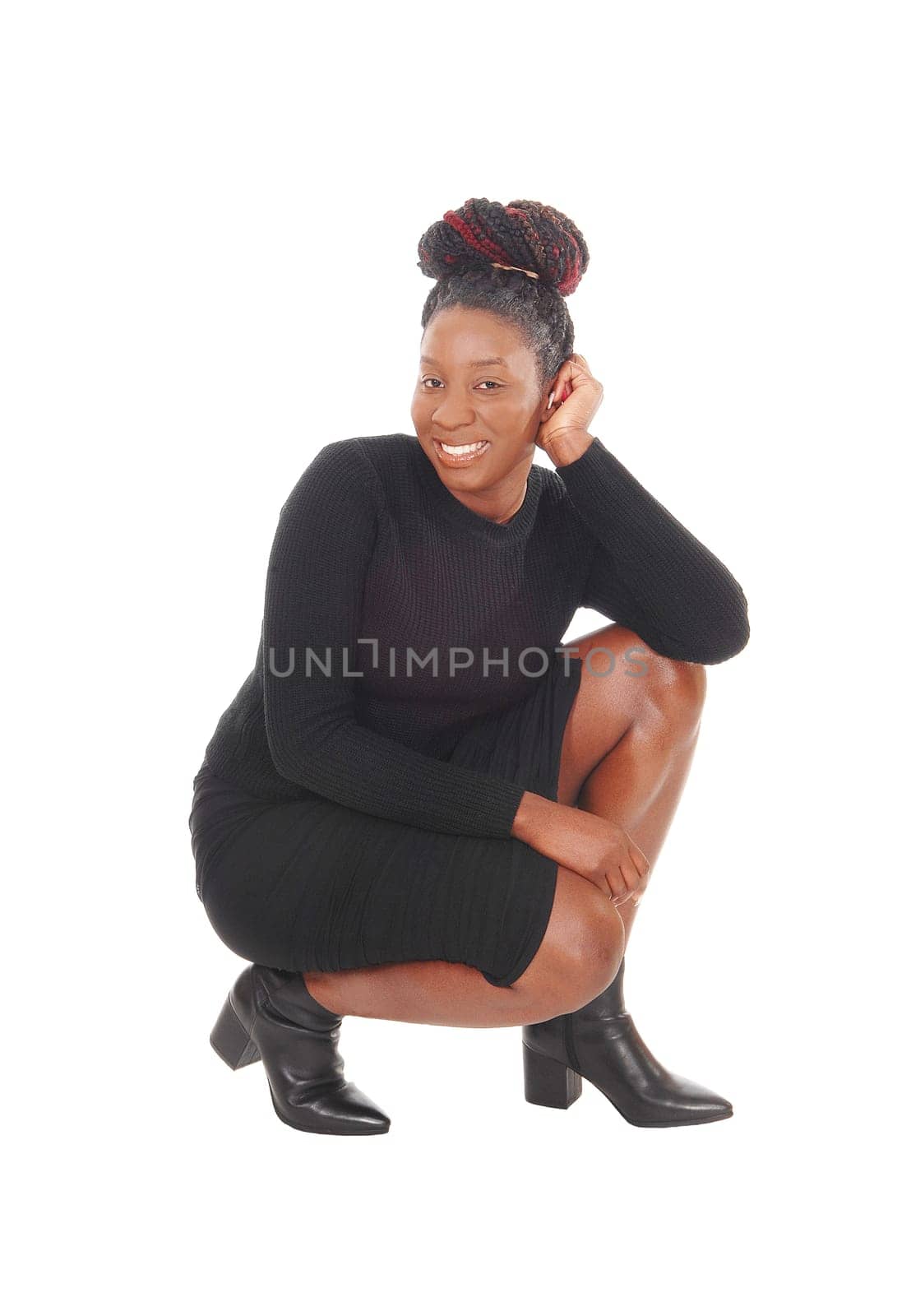 A beautiful African American woman in a black dress crouching on.the floor, smiling, isolated for white background.